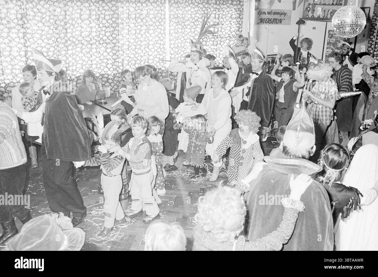 Carnevale per i bambini Hillegom Carnival Hillegom, Whizgle News, Dutch Desk, Paesi Bassi, 1950 - 2000 il 29-02-1984. Questi sono gli argomenti nell'immagine. La scena è piena di attività in un vivace ambiente interno, probabilmente una sala comune o una sala per feste, dove si svolge un evento festivo. Lo spazio è pieno di persone diverse, tra cui bambini e adulti, tutte impegnate in vivaci celebrazioni. I colori sono sorprendenti ma prevalentemente silenziosi, con un tono bianco e nero che crea un'atmosfera nostalgica. Piccoli tocchi di colore emergono dai costumi: Alcuni individui sono vestiti in pla Foto Stock Carnevale per i bambini Hillegom Carnival Hillegom, Whizgle News, Dutch Desk, Paesi Bassi, 1950 - 2000 il 29-02-1984. Questi sono gli argomenti nell'immagine. La scena è piena di attività in un vivace ambiente interno, probabilmente una sala comune o una sala per feste, dove si svolge un evento festivo. Lo spazio è pieno di persone diverse, tra cui bambini e adulti, tutte impegnate in vivaci celebrazioni. I colori sono sorprendenti ma prevalentemente silenziosi, con un tono bianco e nero che crea un'atmosfera nostalgica. Piccoli tocchi di colore emergono dai costumi: Alcuni individui sono vestiti in pla Foto Stock
