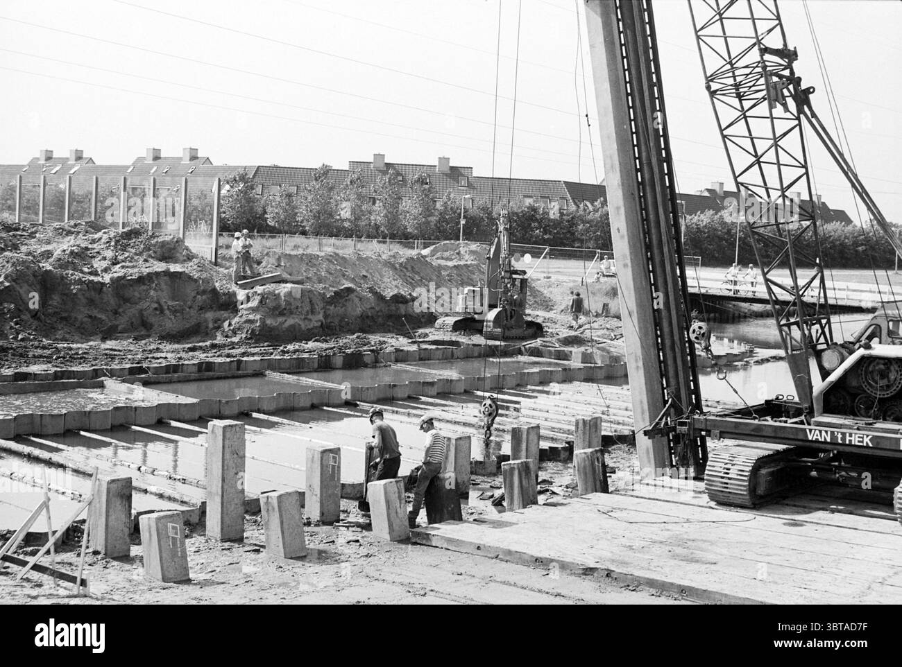 Lavori di costruzione su banchine, Whizgle News, Dutch Desk, Paesi Bassi, 1950 - 2000 il 18-07-1994. L'immagine mostra questi argomenti. La scena cattura un vivace cantiere sotto un cielo luminoso e limpido, con la luce del sole che illumina l'area. Da un lato, una grande gru sovrasta il sito e la sua struttura metallica crea ombre definite e nitide sul terreno. La gru è impegnata attivamente nel sollevamento dei materiali, suggerendo un'atmosfera dinamica. In primo piano, diversi lavoratori sono impegnati a dirigere e gestire le attività. Sono vestiti con abiti da lavoro, come elmetti, guanti e stivali pesanti, a dimostrazione del loro stile Foto Stock