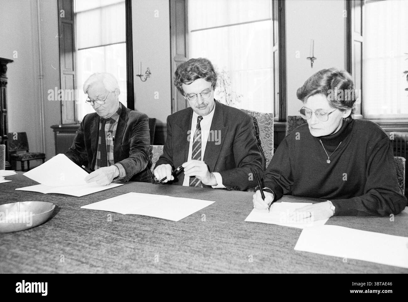 Firma dell'edificio Pabo, Whizgle News, Dutch Desk, Paesi Bassi, 1950 - 2000 il 21-02-1993. Questi argomenti vengono visualizzati nell'immagine. In un ambiente luminoso e spazioso, tre persone sono sedute intorno ad un lungo tavolo di legno scuro ricoperto da fogli di carta. La sala è dotata di ampie finestre che consentono alla luce naturale di filtrare, proiettando ombre morbide sulla superficie del tavolo. A sinistra, una persona con i capelli d'argento è vestita con una camicia bianca e nera a motivi geometrici. Sembrano concentrati, studiano un documento davanti a loro, forse si preparano a firmare o prendere appunti. Al centro c'è un altro dentro Foto Stock