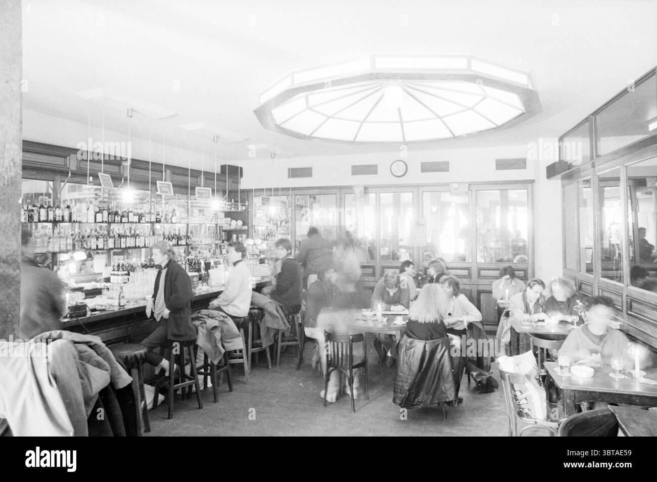 Pub Crawl River Vismarkt Haarlem Cafe Haarlem Riviervismarkt The Netherlands, Whizgle News, Dutch Desk, Paesi Bassi, 1950 - 2000 il 04-04-1986. L'immagine include questi argomenti. La scena cattura l'affollato interno di una caffetteria, caratterizzato da un'arte di mix di modernità e un tocco di stile vintage. L'ambiente è spazioso, con alti soffitti e un prominente lucernario circolare che diffonde luce soffusa e naturale in tutta la sala, contribuendo a creare un'atmosfera invitante. Un lungo bar corre lungo un lato, riempito di una vasta gamma di bottiglie, scintillante sotto l'illuminazione superiore. Gli sgabelli da bar sono oc Foto Stock