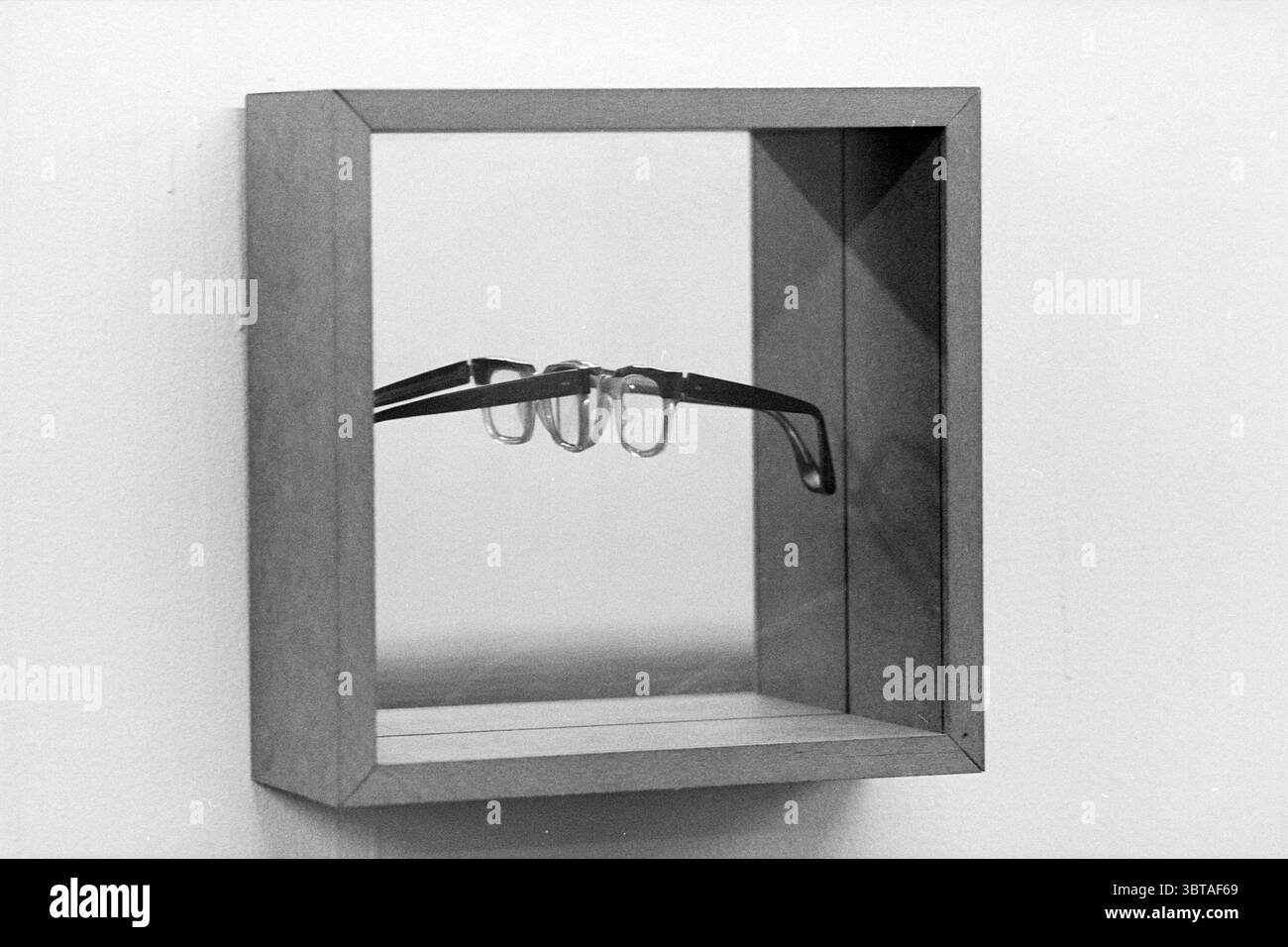Opere d'arte Frans Vendel Vishal Haarlem Grote Markt Nederland, Whizgle News, Dutch Desk, Paesi Bassi, 1950 - 2000 il 07-12-1997. Questi argomenti vengono visualizzati nell'immagine. La scena presenta una semplice ma sorprendente esposizione all'interno di una struttura in legno montata su una parete. La cornice ha una finitura in legno naturale chiaro che le conferisce un'estetica pulita e minimalista. All'interno della cornice, un paio di occhiali si appoggia elegantemente, sostenuto da uno sfondo specchiato. Gli occhiali da vista hanno un design elegante, caratterizzato da cornici scure e leggermente arrotondate che contrastano con la superficie riflettente dietro di loro. Le lenti sono trasparenti, Foto Stock