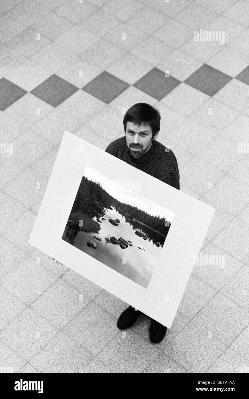 Fossé fotografo RIAGG, Whizgle News, Dutch Desk, Paesi Bassi, 1950 - 2000 il 21-01-1993. Questi sono gli elementi dell'immagine. La scena cattura un uomo in piedi in un'area spaziosa con pavimento piastrellato. Si trova in posizione centrale, con una grande stampa di un tranquillo paesaggio caratterizzato da un corpo d'acqua, circondato da rocce e alberi, che suggerisce una tranquilla scena naturale. L'uomo ha i capelli scuri e la barba, e la sua espressione appare contemplativa. Indossa un maglione scuro testurizzato che aggiunge un senso di calore al suo comportamento. Il contrasto tra luce e ombra mette in risalto le sue caratteristiche e il Foto Stock Fossé fotografo RIAGG, Whizgle News, Dutch Desk, Paesi Bassi, 1950 - 2000 il 21-01-1993. Questi sono gli elementi dell'immagine. La scena cattura un uomo in piedi in un'area spaziosa con pavimento piastrellato. Si trova in posizione centrale, con una grande stampa di un tranquillo paesaggio caratterizzato da un corpo d'acqua, circondato da rocce e alberi, che suggerisce una tranquilla scena naturale. L'uomo ha i capelli scuri e la barba, e la sua espressione appare contemplativa. Indossa un maglione scuro testurizzato che aggiunge un senso di calore al suo comportamento. Il contrasto tra luce e ombra mette in risalto le sue caratteristiche e il Foto Stock