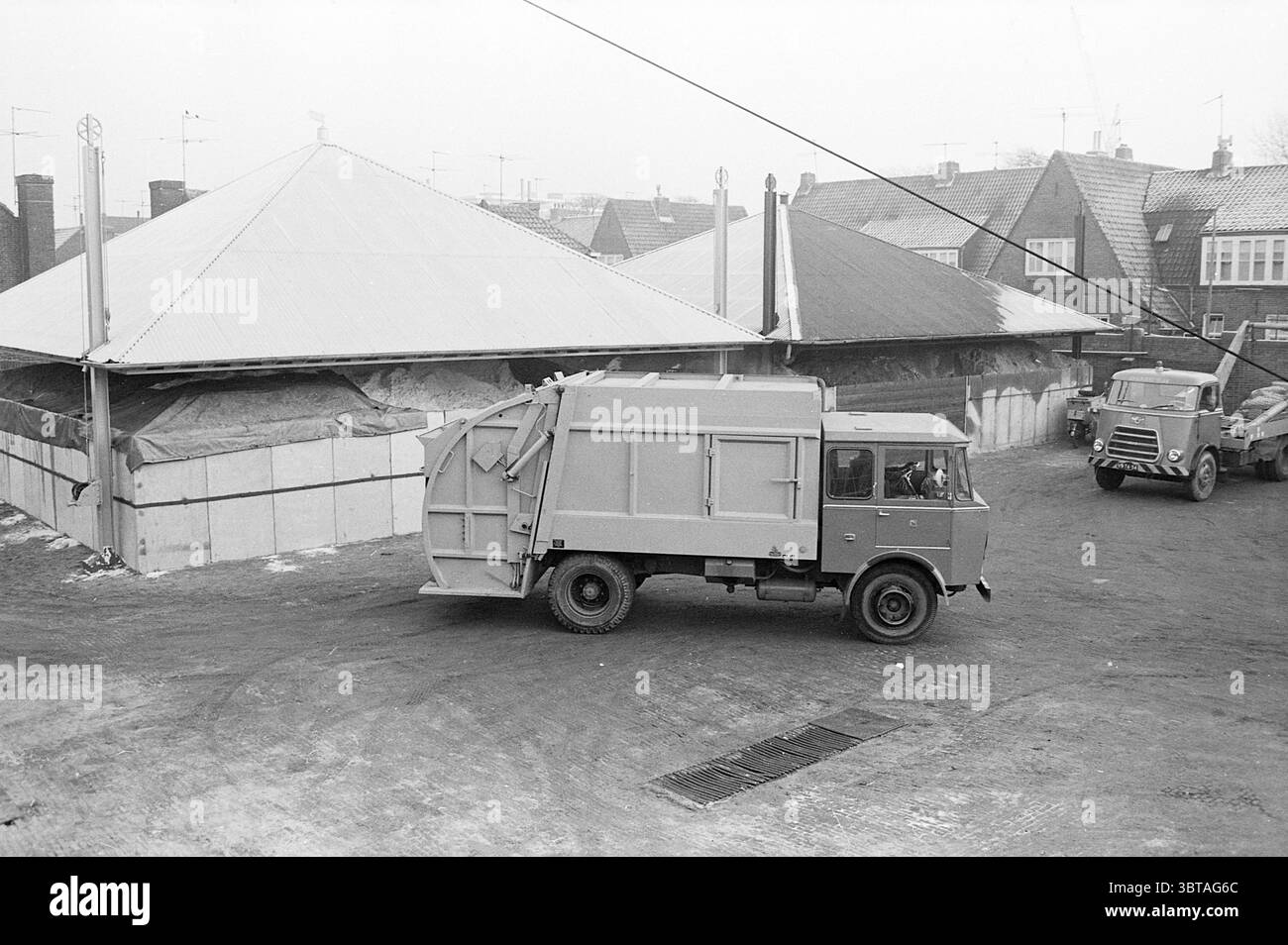 Nuovi veicoli per la pulizia municipale, Whizgle News, Dutch Desk, Paesi Bassi, 1950 - 2000 il 12-12-1968. L'immagine mostra questi argomenti. In questa scena, un veicolo utilitario grigio sta facendo una svolta in un ambiente un po' industriale. Il veicolo ha una forma distinta e boxy con una parte anteriore piatta e un lato esteso e sembra allontanarsi dal visualizzatore. La superficie è umida, il che suggerisce un ambiente umido, probabilmente dovuto alla recente pioggia o alla neve. Intorno al veicolo, l'area è contrassegnata da una combinazione di strutture. A sinistra, un grande edificio circolare con tetto metallico, indicativo di Foto Stock