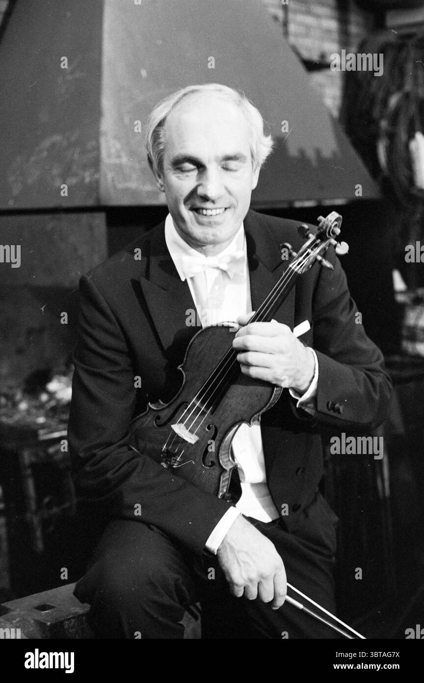 Concerto Smederij van Gaalen e ritratto Gijs Beths concerti musica, Whizgle News, Dutch Desk, Paesi Bassi, 1950 - 2000 il 24-09-1988. Questi sono gli argomenti nell'immagine. In un ambiente caldo e illuminato che suggerisce un incontro intimo, un uomo siede con fiducia, pronto e rilassato. Indossa un classico smoking nero con un papillon bianco, che trasuda eleganza e raffinatezza. L'illuminazione soffusa crea un bagliore lusinghiero sulle sue caratteristiche, evidenziando un sorriso delicato che suggerisce calore e accessibilità. Nelle sue mani, culla un violino, il suo legno lucido luccicante sottilmente sotto la luce. Lo strumento Foto Stock Concerto Smederij van Gaalen e ritratto Gijs Beths concerti musica, Whizgle News, Dutch Desk, Paesi Bassi, 1950 - 2000 il 24-09-1988. Questi sono gli argomenti nell'immagine. In un ambiente caldo e illuminato che suggerisce un incontro intimo, un uomo siede con fiducia, pronto e rilassato. Indossa un classico smoking nero con un papillon bianco, che trasuda eleganza e raffinatezza. L'illuminazione soffusa crea un bagliore lusinghiero sulle sue caratteristiche, evidenziando un sorriso delicato che suggerisce calore e accessibilità. Nelle sue mani, culla un violino, il suo legno lucido luccicante sottilmente sotto la luce. Lo strumento Foto Stock