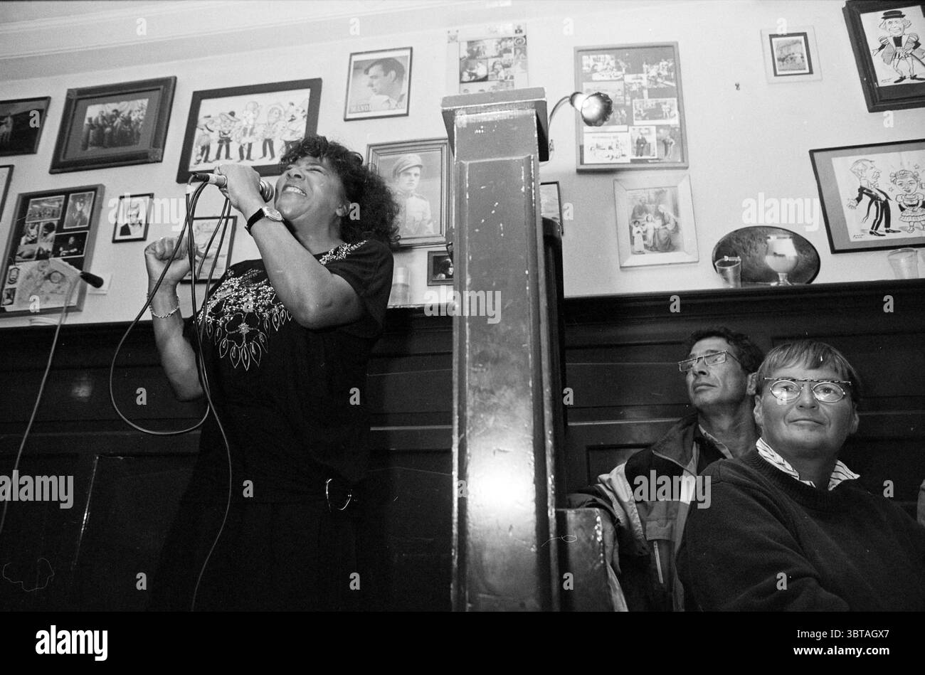 Haarlem Jazz Millie Scott, Whizgle News, Dutch Desk, Paesi Bassi, 1950 - 2000 on 26-08-1993. L'immagine contiene questi argomenti. In una stanza accogliente e poco illuminata piena di nostalgia, una donna sta in prima linea, cantando appassionatamente in un microfono. Il suo volto espressivo è illuminato da emozioni, incorniciato da capelli ricci che aggiungono una qualità dinamica alla sua presenza. Indossa un capo scuro ornato da ricami intricati, che contrastano splendidamente con i colori caldi dell'arredamento circostante. Dietro di lei, una colonna in legno fornisce un supporto strutturale allo spazio e aggiunge al fascino rustico del se Foto Stock
