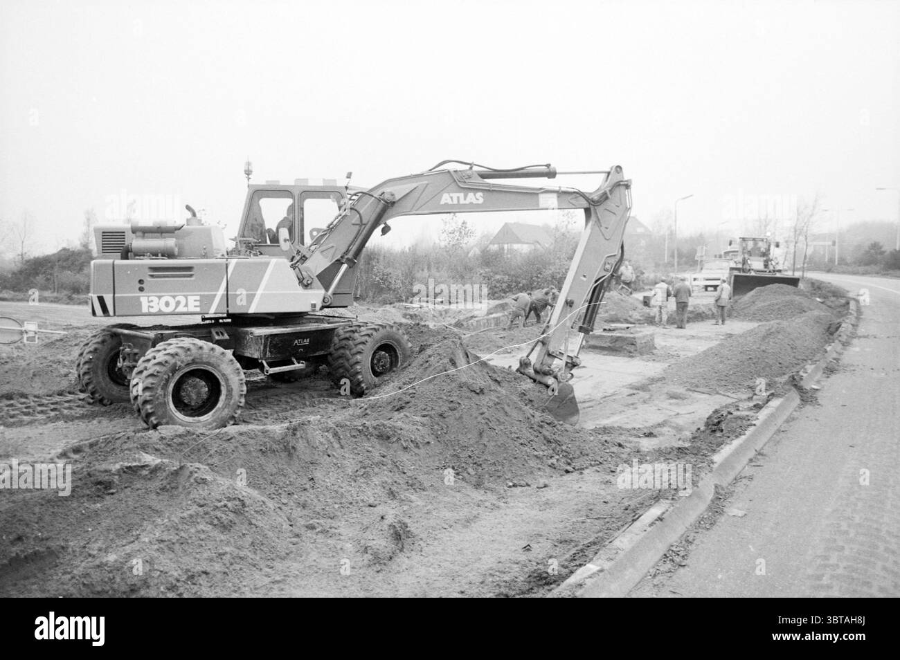 Activities Van de Endelaan Hillegom Activities Hillegom Van den Endelaan, Whizgle News, Dutch Desk, Paesi Bassi, 1950 - 2000 il 25-10-1988. Questi argomenti sono mostrati nell'immagine. La scena raffigura un cantiere caratterizzato dalla presenza di macchinari pesanti e da un processo di scavo in corso. In primo piano, si erge un importante escavatore, la sua struttura metallica verniciata in tonalità di grigio e arancione, che mostra l'usura derivante da un uso costante. I cingoli dei macchinari sono in profondità nella terra ammutinata, circondati da mucchi di terra e sabbia, il che suggerisce una quantità significativa di attività recenti. Da a. Foto Stock