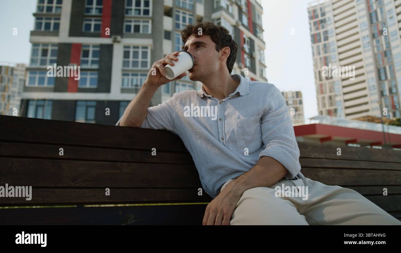 Uomo europeo caucasico seduto sulla panchina maschio che tiene tazza pausa caffè bere takeaway ordine cliente acquirente rilassarsi gustoso drink Guy studente uomo d'affari Foto Stock