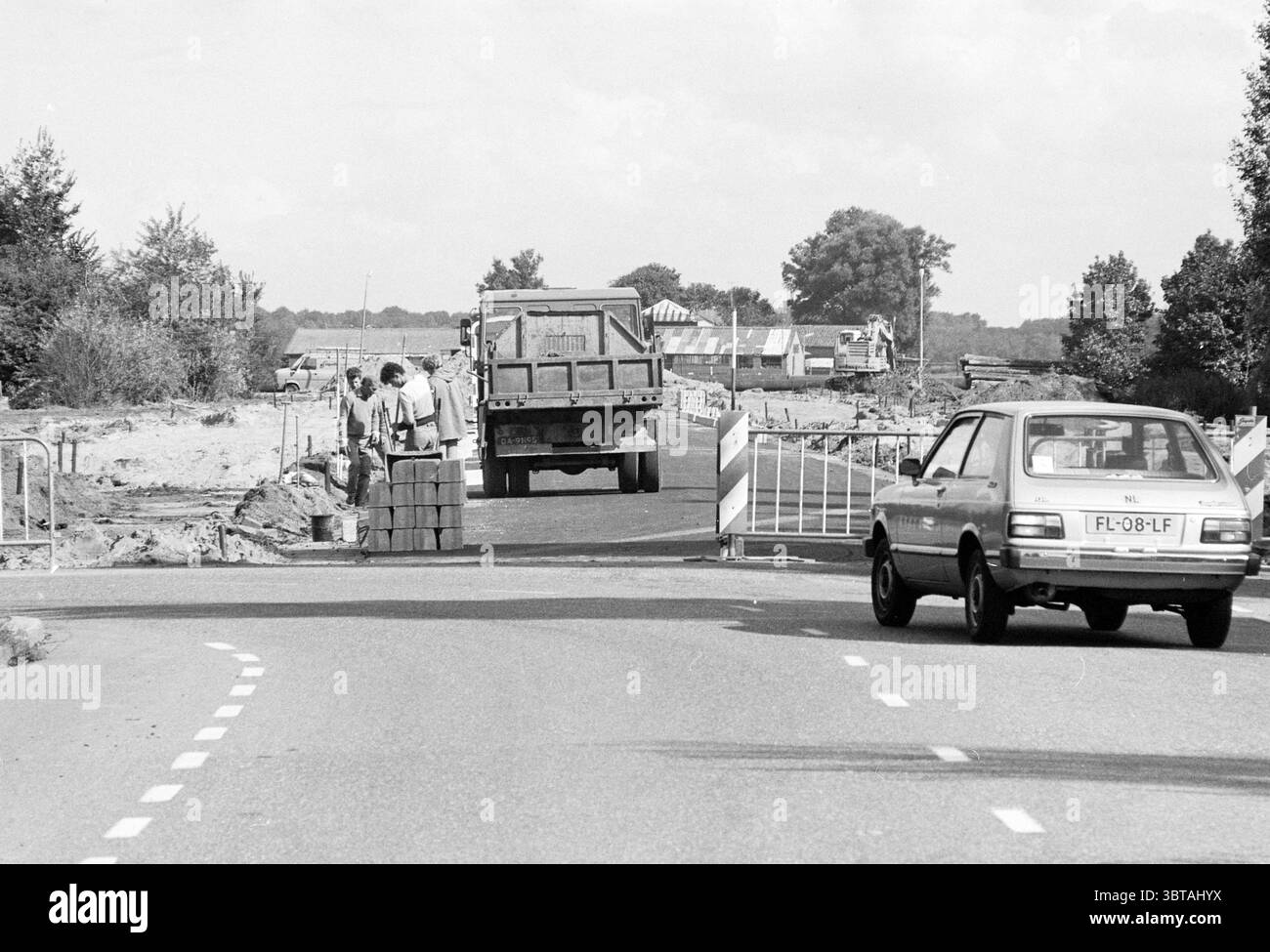 Estensione di Hillinenweg Hillegom Hillegom costruzione di strade messa a terra di Hillegom Hillinenweg, Whizgle News, Dutch Desk, Paesi Bassi, 1950 - 2000 il 06-09-1984. Questi sono gli elementi dell'immagine. La scena raffigura un cantiere lungo una strada. In primo piano, una strada stretta si divide in due corsie, con un piccolo veicolo, una berlina di vecchio modello, che guida verso sinistra. L'auto è di colore neutro, probabilmente grigio o azzurro, e ha un design compatto tipico dei veicoli più vecchi. Sul lato destro della strada, un camion di grandi dimensioni, forse un camion ribaltabile, si sta riversando verso un mucchio di manto stradale Foto Stock