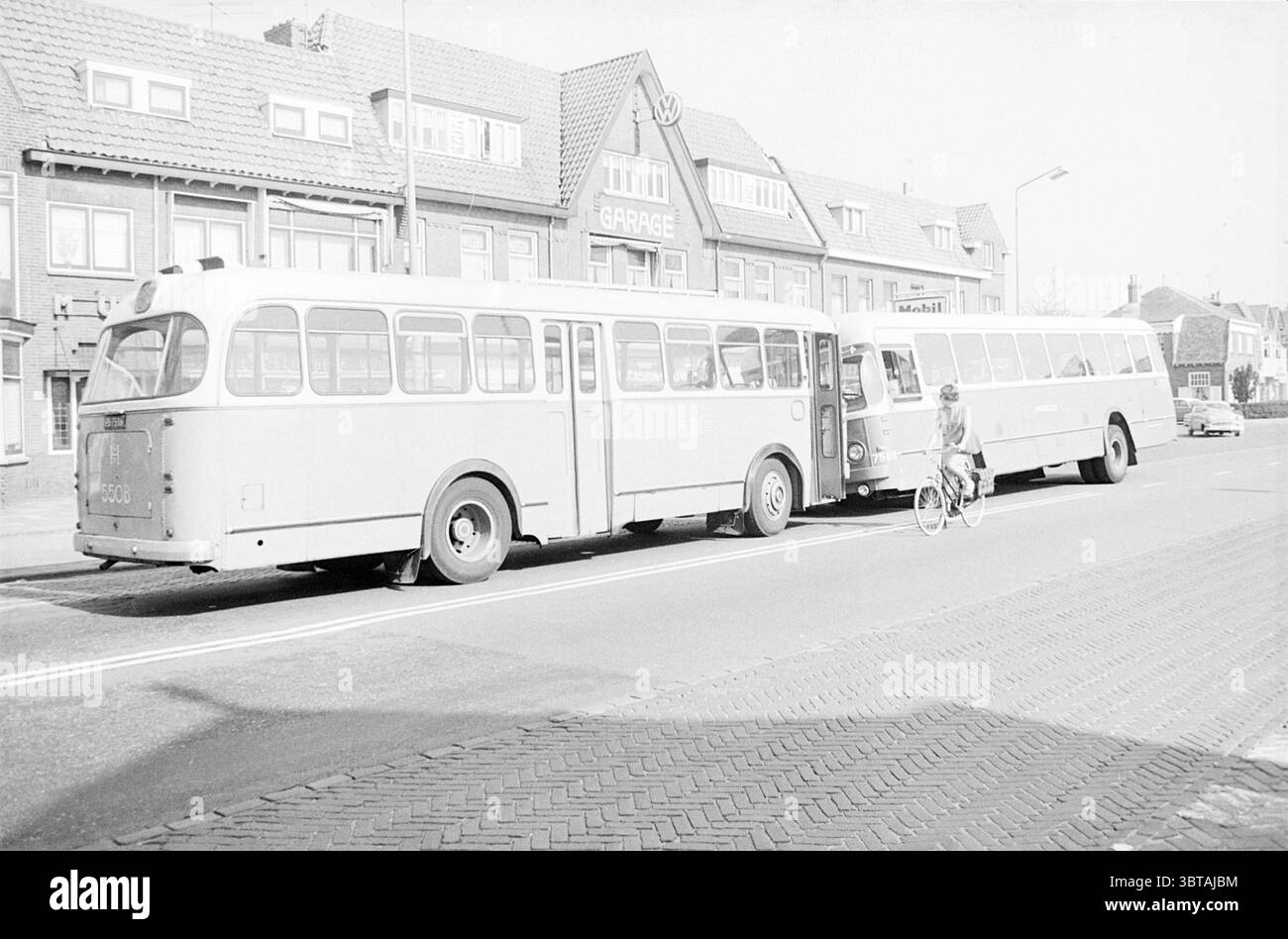 Autobus NACO con assale rotto Naco, Whizgle News, Dutch Desk, Paesi Bassi, 1950 - 2000 il 10-04-1967. L'immagine contiene questi argomenti. Nella scena, due grandi autobus sono parcheggiati fianco a fianco su un'ampia strada asfaltata, creando un'immagine sorprendente del trasporto pubblico urbano. Gli autobus mostrano una tonalità pastello, probabilmente un blu pallido o un grigio chiaro, che contrasta leggermente con l'architettura più tradizionale sullo sfondo. L'ambiente presenta edifici in mattoni con tetti a falda, molto probabilmente di epoca metà del XX secolo, che mostrano un mix di toni neutri e alcuni elementi accentati. Un edificio si distingue Foto Stock