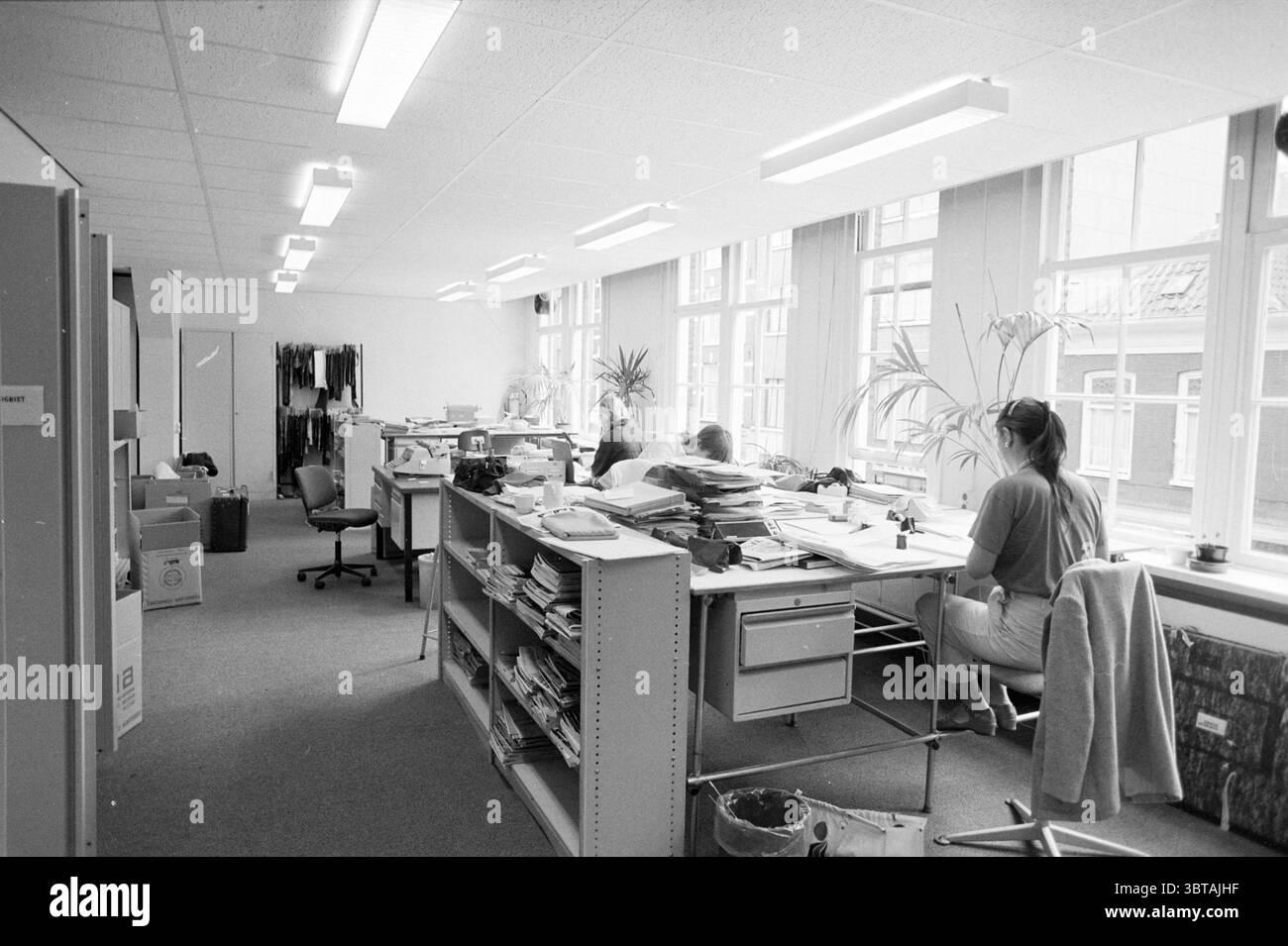 Interno del nuovo edificio VNU Amsterdam interno VNU Associazione degli editori olandesi Amsterdam Paesi Bassi, Whizgle News, Dutch Desk, Paesi Bassi, 1950 - 2000 il 17-07-1980. L'immagine include questi argomenti. La scena è ambientata in un ambiente di ufficio spazioso, caratterizzato da una disposizione ordinata di scrivanie e scaffali. Le pareti sono dipinte in un chiaro tono neutro, permettendo alla luce naturale di inondarsi dalle grandi finestre su un lato. Queste finestre si estendono quasi dal pavimento al soffitto, proiettando ombre morbide in tutta la stanza, evidenziando la luminosità dello spazio. In primo piano, una c Foto Stock