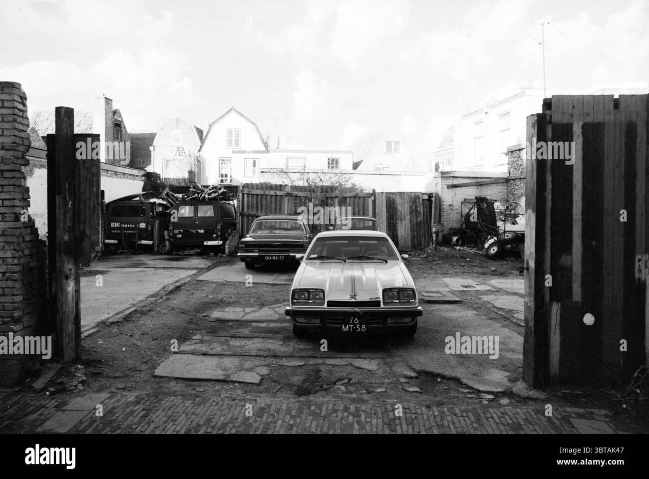Parcheggio deteriorato vicino a De Witstraat Haarlem Paesi Bassi, Whizgle News, Dutch Desk, Paesi Bassi, 1950 - 2000 il 20-11-1978. L'immagine mostra questi argomenti. La scena cattura un paesaggio urbano desolato, caratterizzato principalmente da un'area aperta dominata da un paio di auto parcheggiate. Questi veicoli, invecchiati e leggermente arrugginiti, occupano una posizione centrale su una superficie spaccata e ricoperta di ghiaia. Ogni auto sembra mostrare segni di usura, con vernice sbiadita e un senso di negligenza. Intorno alle auto c'è un ambiente robusto con una miscela di resti industriali. Sullo sfondo, diverse strutture fatiscenti Foto Stock