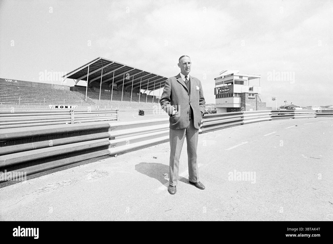Sig. Hugenholtz al circuito di Zandvoort persone Zandvoort Burgemeester van Alphenstraat, Whizgle News, Dutch Desk, Paesi Bassi, 1950 - 2000 il 05-06-1973. Questi argomenti vengono visualizzati nell'immagine. In questa scena, un uomo si erge in sicurezza su un circuito, circondato dai resti di una vibrante atmosfera di sport motoristici. È vestito con un abito grigio sartoriale, trasuda un senso di eleganza e professionalità, e il suo comportamento suggerisce una miscela di orgoglio e contemplazione. L'autodromo si estende dietro di lui, segnato da linee bianche distinte che delineano le corsie. Lo sfondo rivela una tribuna, che Foto Stock