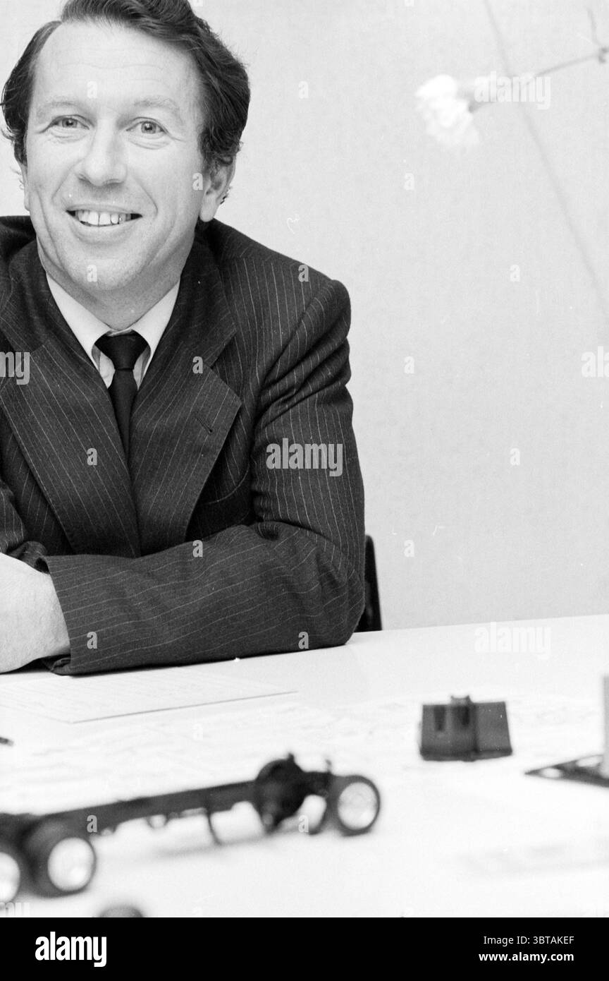 Ritratto di Korevaar Hillegom Portraits Hillegom, Whizgle News, Dutch Desk, Paesi Bassi, 1950 - 2000 il 23-10-1980. Questi sono gli argomenti nell'immagine. La scena vede un uomo con un'espressione allegra, seduto a un tavolo. È vestito con una tuta scura di pinstripe che contrasta con lo sfondo più chiaro e neutro. I suoi capelli sono scuri e ben modellati, e ha un sorriso caldo che suggerisce l'avvicinabilità. Sul tavolo di fronte a lui, ci sono piccoli oggetti che sembrano essere componenti o modelli, possibilmente correlati alla progettazione meccanica o all'ingegneria, che indicano un punto focale dell'area di lavoro Foto Stock