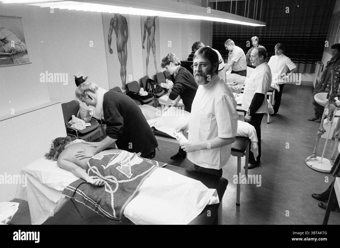 Formazione massaggiatore Sig. Kollaart e formazione studentesca Haarlem Kleine Houtweg Paesi Bassi, Whizgle News, Dutch Desk, Paesi Bassi, 1950 - 2000 il 20-02-1987. Questi sono gli argomenti nell'immagine. La scena raffigura una stanza ben illuminata piena di attività incentrata sul tema del massaggio terapeutico o del bodywork. L'ambiente è principalmente interno, caratterizzato da una combinazione di illuminazione soffusa e finestre che consentono alla luce naturale di filtrare, creando un'atmosfera calda ma clinica. In primo piano, diversi tavoli di trattamento sono disposti in parallelo, ciascuno rivestito di lino bianco Foto Stock