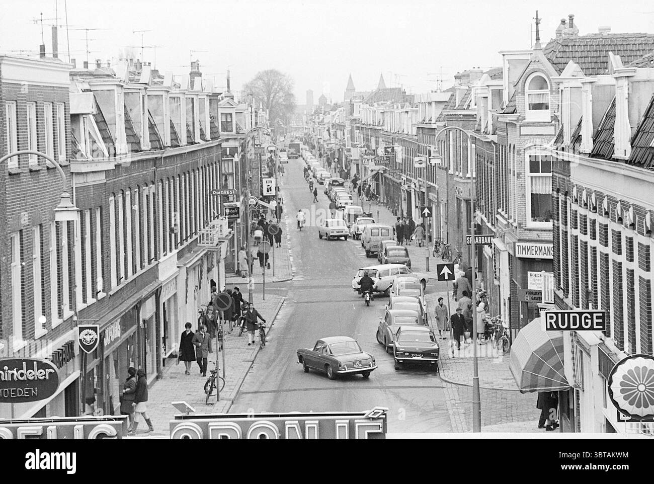 Panoramica Cronjéstraat Overviews Haarlem Generaal Cronjéstraat Paesi Bassi, Whizgle News, Dutch Desk, Paesi Bassi, 1950 - 2000 il 04-03-1968. Questi argomenti vengono visualizzati nell'immagine. La scena raffigura una vivace strada urbana, fiancheggiata da affascinanti edifici in mattoni che presentano un mix di tetti spioventi, ognuno decorato con varie sfumature di cornici e tende da sole. L'architettura riflette una miscela di stili, contribuendo a creare un'atmosfera pittoresca ma vivace. In primo piano, un gruppo eterogeneo di persone attraversa la strada. Alcuni sono impegnati in conversazione, mentre altri sembrano essere in transito, creatina Foto Stock