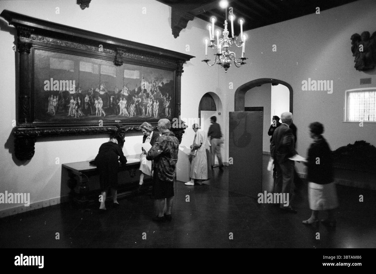 Orchestra a lume di candela in Frans Hals Orchestras Haarlem Groot Heiligland Nederland, Whizgle News, Dutch Desk, Paesi Bassi, 1950 - 2000 il 20-05-1988. L'immagine contiene questi argomenti. La scena è ambientata in una galleria spaziosa ed elegante con alti soffitti ed elementi architettonici classici. Le pareti sono dipinte di bianco tenue, creando uno sfondo pulito che contrasta con i ricchi toni delle opere d'arte esposte in modo prominente. Una grande cornice ornata racchiude un dipinto drammatico, brulicante di figure impegnate in una scena espressiva, che probabilmente ritrae una narrazione storica o mitologica. S Foto Stock