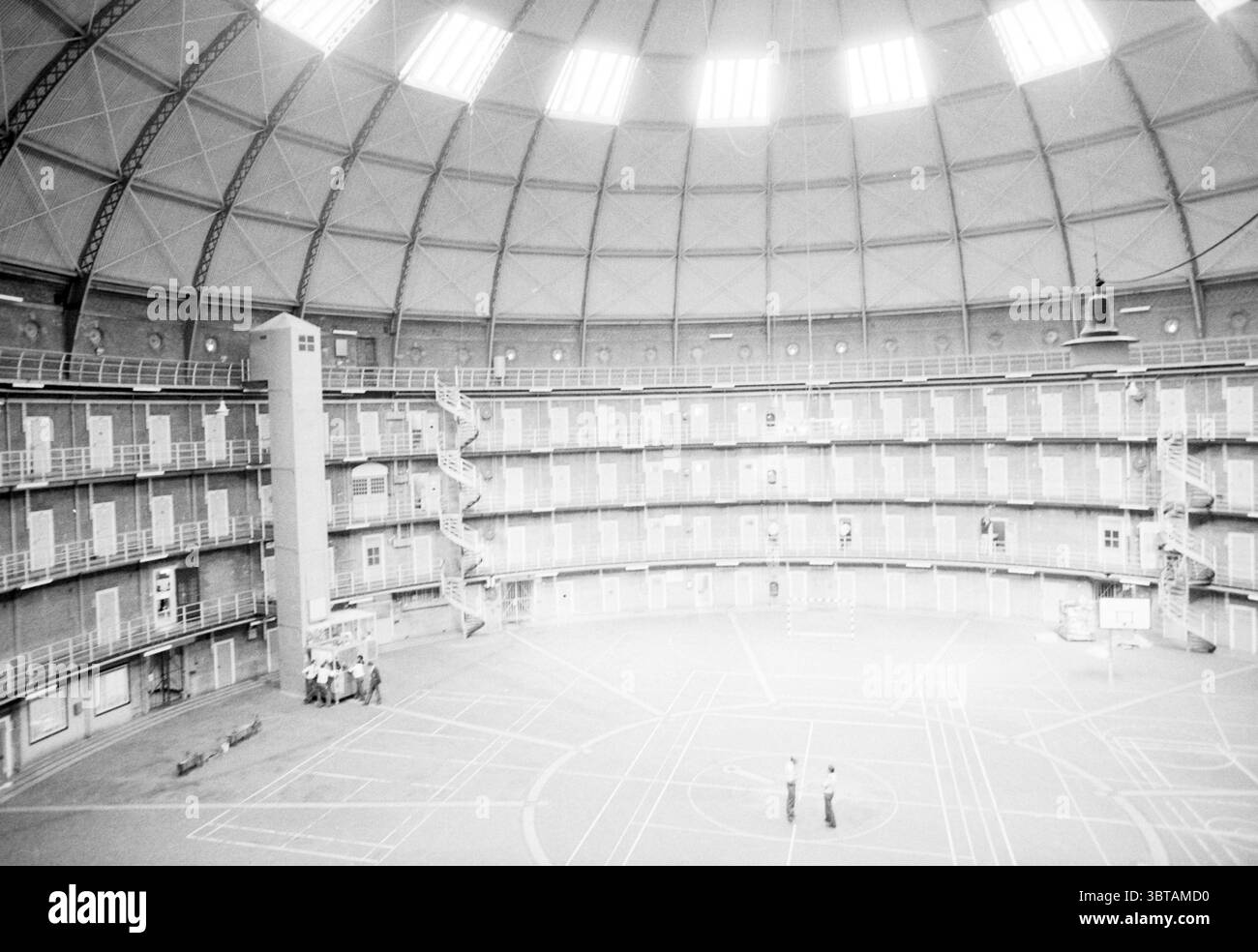 Prigione interna "dome" Haarlem Prison Haarlem Paesi Bassi, Whizgle News, Dutch Desk, Paesi Bassi, 1950 - 2000 il 09-09-1983. L'immagine mostra questi argomenti. La scena presenta un ampio spazio circolare con torreggianti pareti in mattoni a vista. L'architettura presenta un suggestivo soffitto a cupola, caratterizzato da una serie di intricati motivi geometrici creati da travi metalliche che si irradiano da un punto centrale sopra. La luce naturale filtra attraverso un anello di sfiati vicino all'apice, diffondendo un'illuminazione morbida e diffusa nell'area. Alla base, il pavimento è contrassegnato da linee distinte, lik Foto Stock