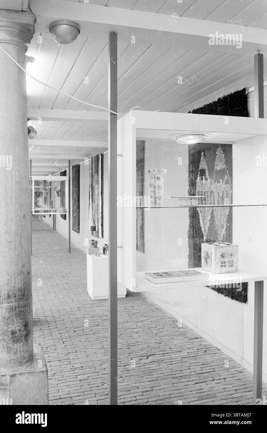 Mostra Vishal arazzi finlandesi mostre, Whizgle News, Dutch Desk, Paesi Bassi, 1950 - 2000 il 07-06-1966. Questi sono gli argomenti nell'immagine. La scena presenta un interno spazioso caratterizzato da un lungo corridoio fiancheggiato da esposizioni. Il pavimento è composto da mattoni pallidi, creando un ambiente caldo ma silenzioso che contrasta con gli elementi più moderni della presentazione. Su un lato del corridoio, alte colonne sostengono un soffitto adornato da semplici pannelli bianchi. Le pareti sono rivestite di tessuti testurizzati, che aggiungono profondità e una qualità tattile all'ambiente. Questi materiali fea Foto Stock