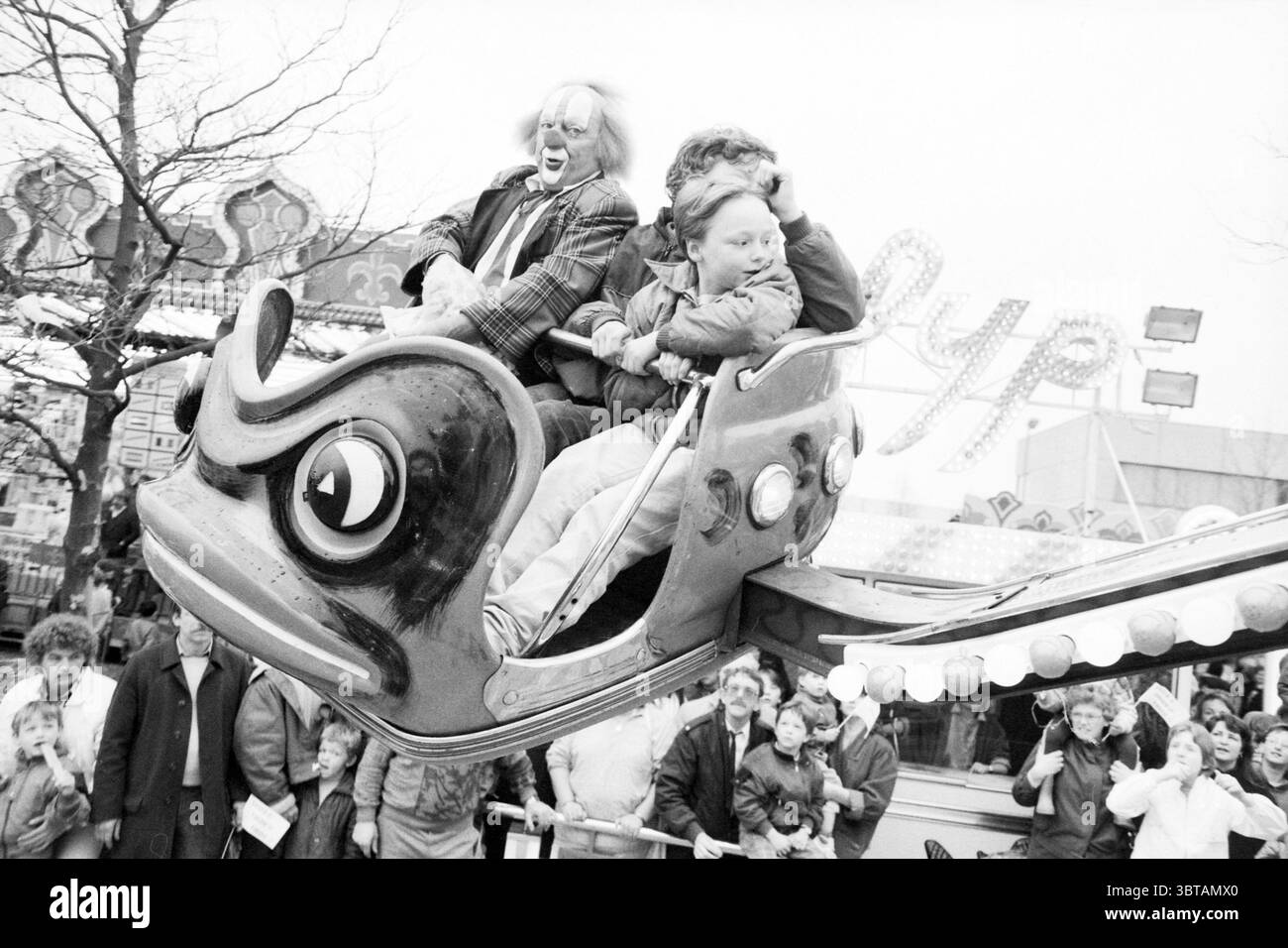 Bassie e Adriaan alla fiera Schalkwijk Fair Performance Haarlem Paesi Bassi, Whizgle News, Dutch Desk, Paesi Bassi, 1950 - 2000 il 27-04-1986. Questi sono gli argomenti nell'immagine. La scena cattura l'emozione di un'atmosfera carnevalesca, dove colori vivaci e movimento dinamico creano un'esperienza visiva coinvolgente. In primo piano, una stravagante corsa a forma di grande rana cartonata domina la composizione. Questo giocoso macchinario è principalmente dipinto in verde brillante e accentuato da allegri rossi e gialli, che ne esaltano la natura stravagante. I posti seduti durante la corsa sono t Foto Stock