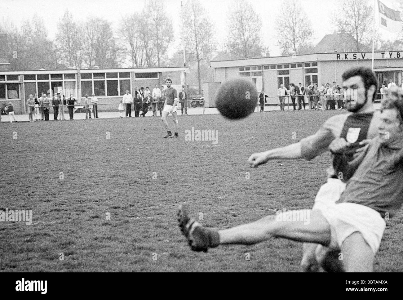 Van Nispen - Lisse Football, Whizgle News, Dutch Desk, Paesi Bassi, 1950 - 2000 il 10-05-1970. Questi sono gli argomenti nell'immagine. La scena cattura un momento di sport all'aperto ambientato su un campo erboso, probabilmente durante una partita di calcio. L'erba è un verde ricco, con macchie di terra marrone visibili, che indicano l'usura del gioco. In primo piano, due giocatori sono attivamente impegnati: Uno sta per entrare in contatto con la palla usando un calcio drammatico, mentre l'altro è in posizione difensiva, apparentemente cercando di bloccare il gioco. I giocatori indossano le classiche divise da calcio, con maniche corte e pantaloncini corti. TH Foto Stock