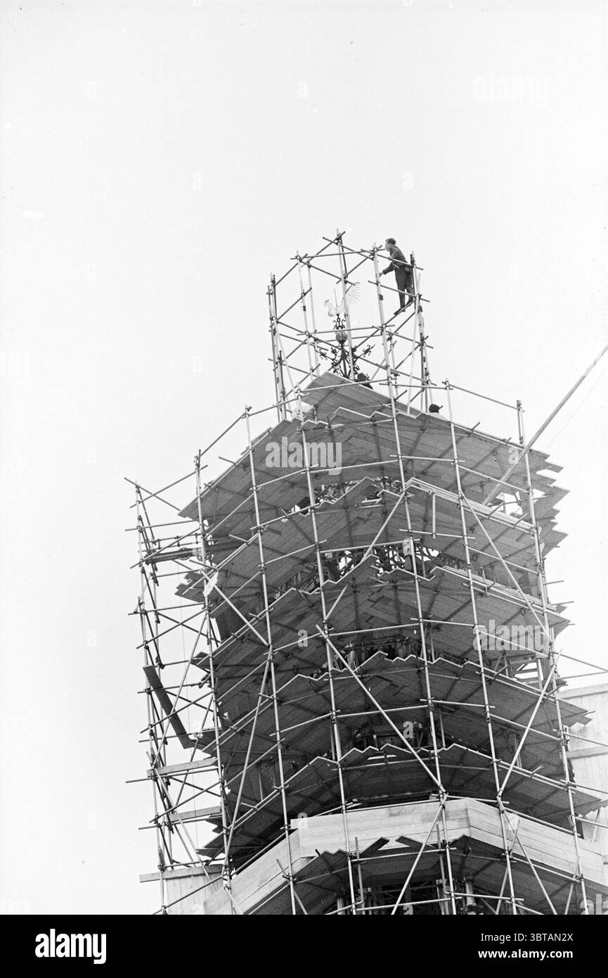 Colleziona la croce e il gallo Grote o Sint-Bavokerk Grote Kerk Haarlem chiese St. Bavokerk Haarlem Grote Markt Paesi Bassi, Whizgle News, Dutch Desk, Paesi Bassi, 1950 - 2000 on 30-06-1964. Questi argomenti sono mostrati nell'immagine. La scena presenta un'alta struttura parzialmente costruita avvolta da impalcature. L'impalcatura, fatta di pali metallici e tavole di legno, crea un motivo simile a una rete che avvolge l'edificio. All'apice, si vede un lavoratore, dotato di un'imbracatura di sicurezza, incentrata sulle attività legate alla struttura dell'edificio. La sua silhouette spicca contro Foto Stock