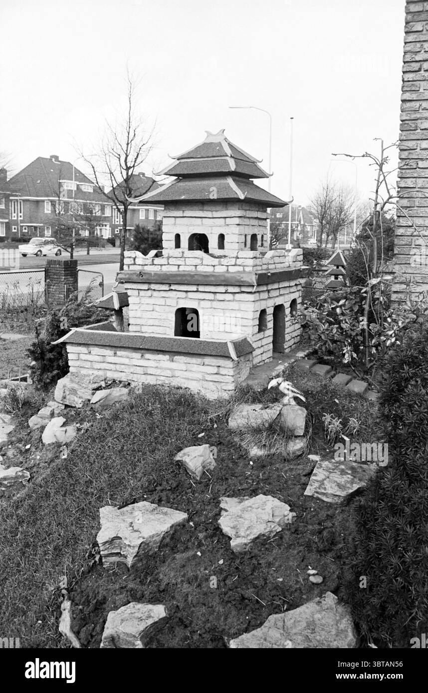 Giardino del tempio cinese, Whizgle News, Dutch Desk, Paesi Bassi, 1950 - 2000 il 02-1964. Questi argomenti vengono visualizzati nell'immagine. La scena presenta una piccola struttura dal design complesso che ricorda una pagoda asiatica, costruita in pietra di colore chiaro. Questa struttura ha un tetto a più livelli con grondaie curve, elegantemente rifinita con tenaglie scure. Si erge in modo prominente in un giardino, circondato da un mix di rocce e vegetazione, aggiungendo un'atmosfera organica alla scena. In primo piano, pietre irregolari sono sparse per il terreno, contribuendo a un aspetto naturale e rustico. Intorno al pagode Foto Stock