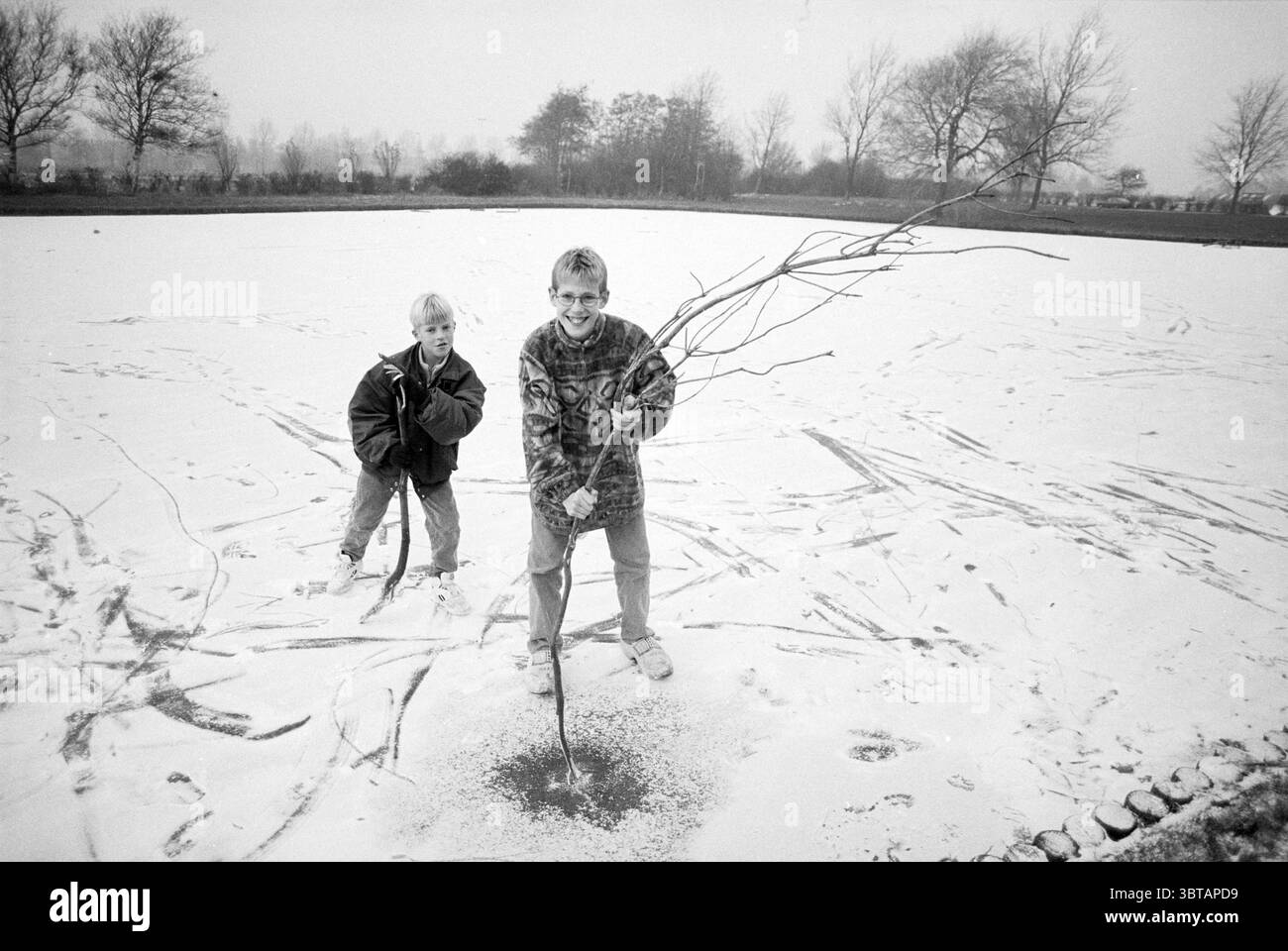 Ice Fun Santpoort Santpoort, Whizgle News, Dutch Desk, Paesi Bassi, 1950 - 2000 su 21-11-1993. Questi argomenti sono mostrati nell'immagine. In un tranquillo paesaggio invernale, due bambini giocano in un campo innevato che si estende davanti a loro. Il terreno è coperto da una morbida e bianca coperta di neve, che risplende sotto la luce del giorno. Il cielo è ricoperto da una tonalità grigia che esalta l'atmosfera invernale. Un bambino, posizionato in primo piano, si erge con sicurezza tenendo diversi ramoscelli lunghi che ha raccolto, pronti a creare qualcosa dalla sua scoperta. Sta indossando un patte Foto Stock