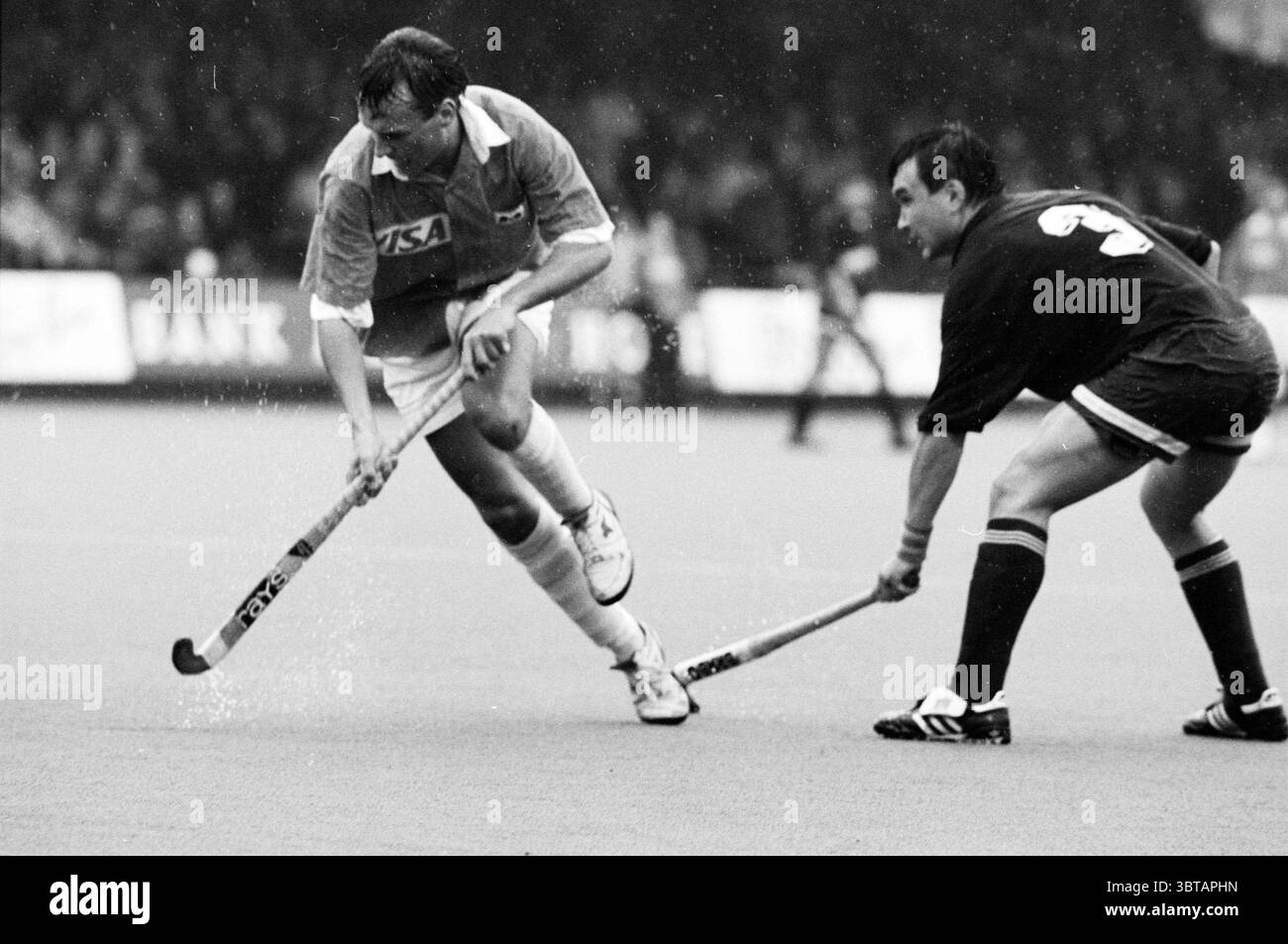 Hockey: Bloemendaal - Alma Ata Bloemendaal, Whizgle News, Dutch Desk, Paesi Bassi, 1950 - 2000 il 16-04-1992. L'immagine mostra questi argomenti. Nella scena, due atleti sono impegnati in un gioco dinamico su un campo, probabilmente durante una partita di hockey. Il giocatore di sinistra, con una maglia di colore chiaro, è in movimento, si piega in avanti mentre manovra abilmente un bastone da hockey. Il suo corpo è leggermente trasformato, enfatizzando la sua concentrazione e agilità. L'altro giocatore, rivestito con un'uniforme scura, è posizionato a destra, concentrandosi con attenzione sull'avversario in arrivo. Il terreno è una surfa silenziosa e strutturata Foto Stock