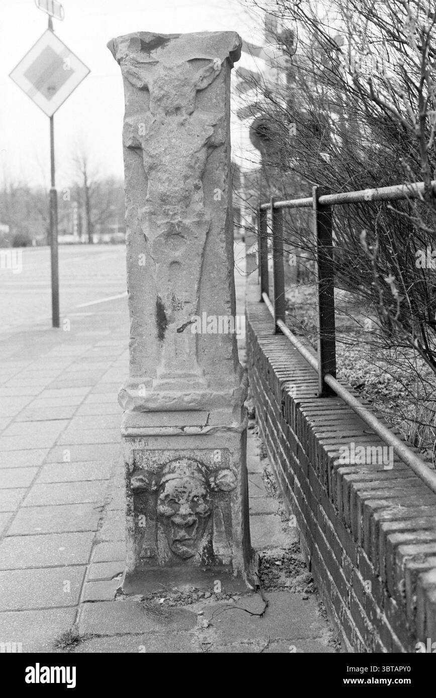 Fence Wüstelaan santpoort Fences Santpoort Wüstelaan, Whizgle News, Dutch Desk, Paesi Bassi, 1950 - 2000 il 17-02-1989. Questi argomenti vengono visualizzati nell'immagine. La scena presenta una colonna di pietra intemprata situata lungo un sentiero vicino a una strada trafficata. Il pilastro si erge in posizione verticale e mostra intricate incisioni, tra cui una figura che sembra raffigurare elementi simili a quelli umani e forse alcuni elementi simbolici. Alla base del pilastro c'è un volto distinto, che rappresenta forse una figura mitica o grottesca, caratterizzata da caratteristiche esagerate che evocano un senso di intrigo. Intorno al pilastro, Th Foto Stock