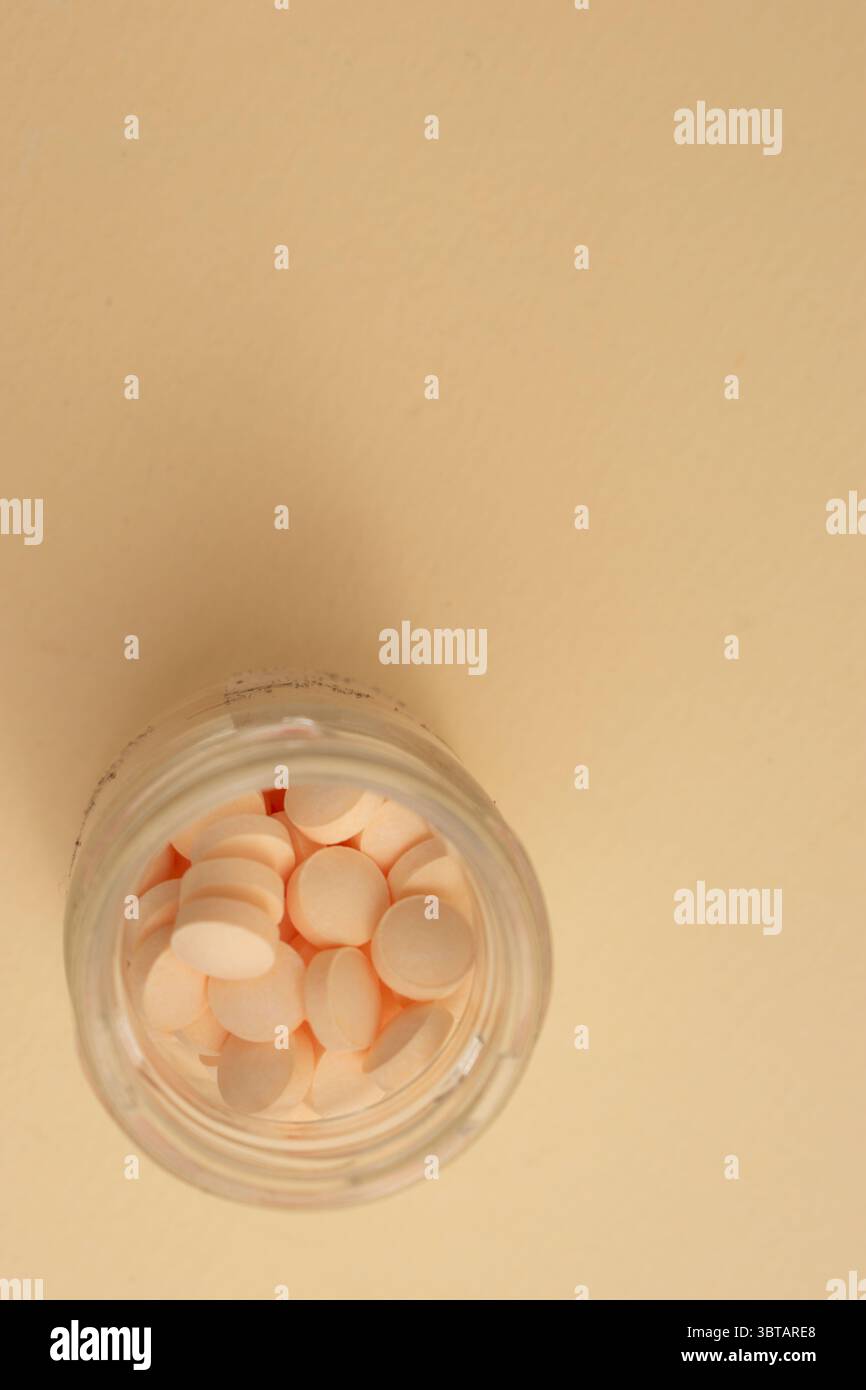Concetto minimalista con pillole rotonde bianche in contenitore di vetro e cucchiaio su sfondo beige Foto Stock