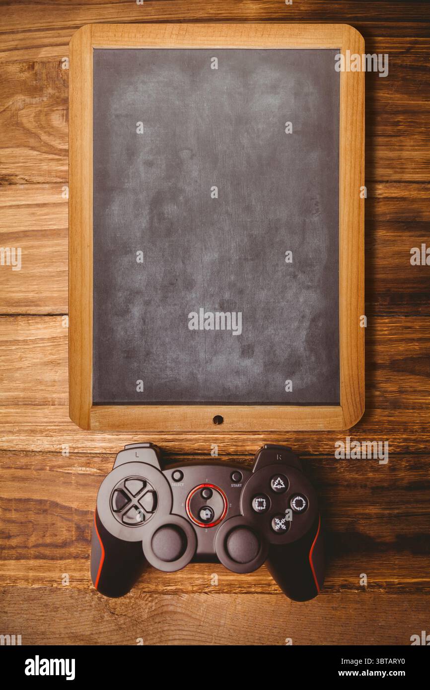 Vettore piatto che mostra una lavagna vuota con cornice in legno sul piano con controller di gioco nero e rosso Foto Stock