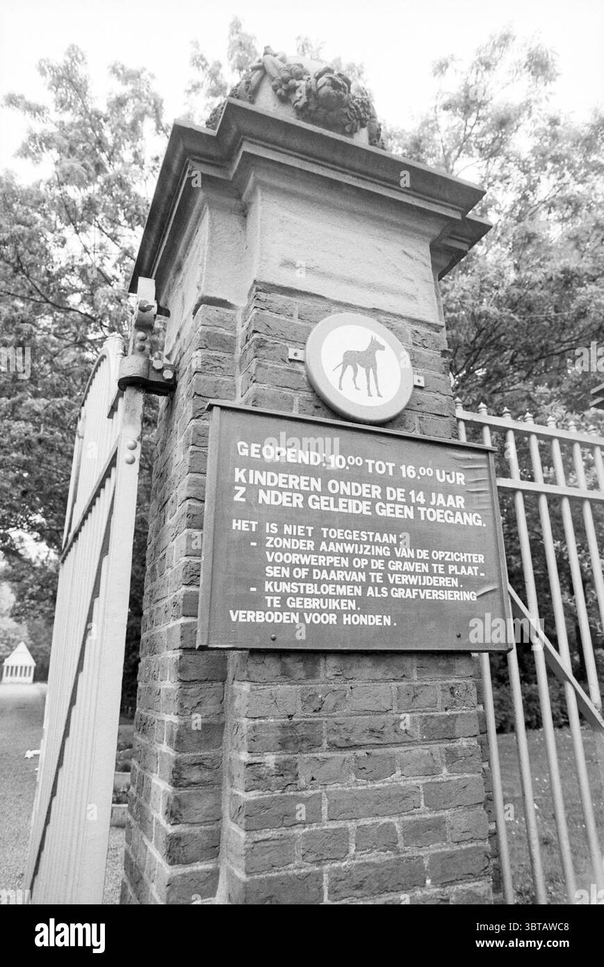 Cartello al cimitero di Kleverlaan Haarlem Kleverlaan Paesi Bassi, Whizgle News, Dutch Desk, Paesi Bassi, 1950 - 2000 il 24-06-1991. Questi sono gli argomenti nell'immagine. Nella scena, un muro di mattoni robusto si erge alto, formando un confine intorno a quello che sembra essere un giardino o un'area esterna. I mattoni hanno una tonalità ricca e profonda, che offre un contrasto con la vibrante vegetazione che emerge dall'alto. All'ingresso, un cancello in ferro battuto è progettato in modo complesso, con forme curve che dividono lo spazio. Il cancello è parzialmente aperto, invitando un senso di esplorazione. Sopra di esso, un emblema decorativo di un cavallo Foto Stock