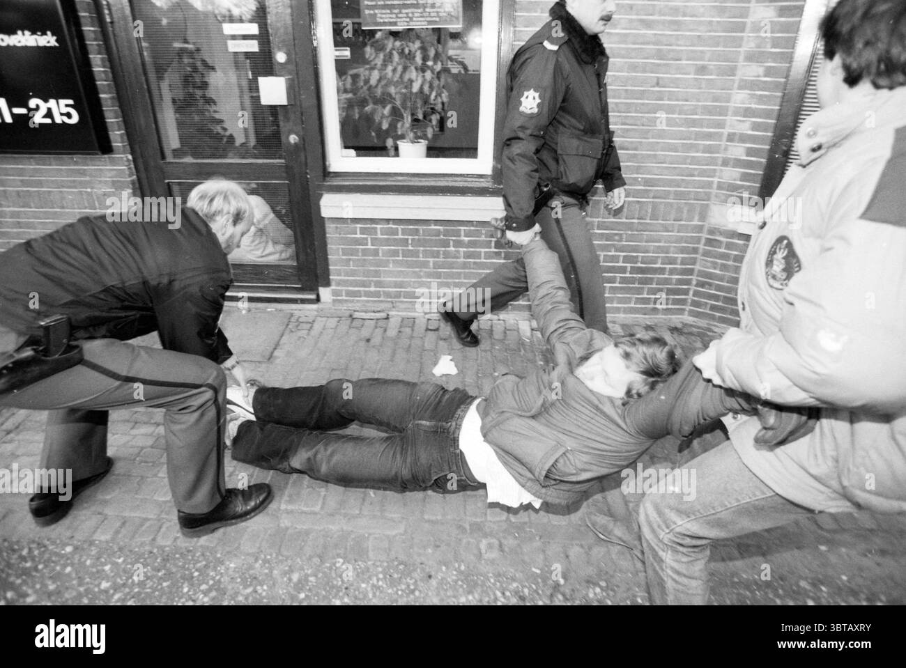 Ontr@@ Bloemenhovekliniek [evacuate], Whizgle News, Dutch Desk, Paesi Bassi, 1950 - 2000 il 16-01-1991. Questi sono gli elementi dell'immagine. La scena raffigura un momento teso su una strada della città. Diverse persone sono coinvolte in una lotta, con una persona seduta a terra, visibilmente in angoscia. Il loro linguaggio del corpo suggerisce resistenza, mentre si piegano all'indietro, allontanandosi da coloro che cercano di aiutarli o di frenarli. La persona a terra indossa un abbigliamento casual, che appare leggermente disinvolto, con jeans denim e un top di colore chiaro. Altre due figure, una con una giacca scura e l'altra Foto Stock