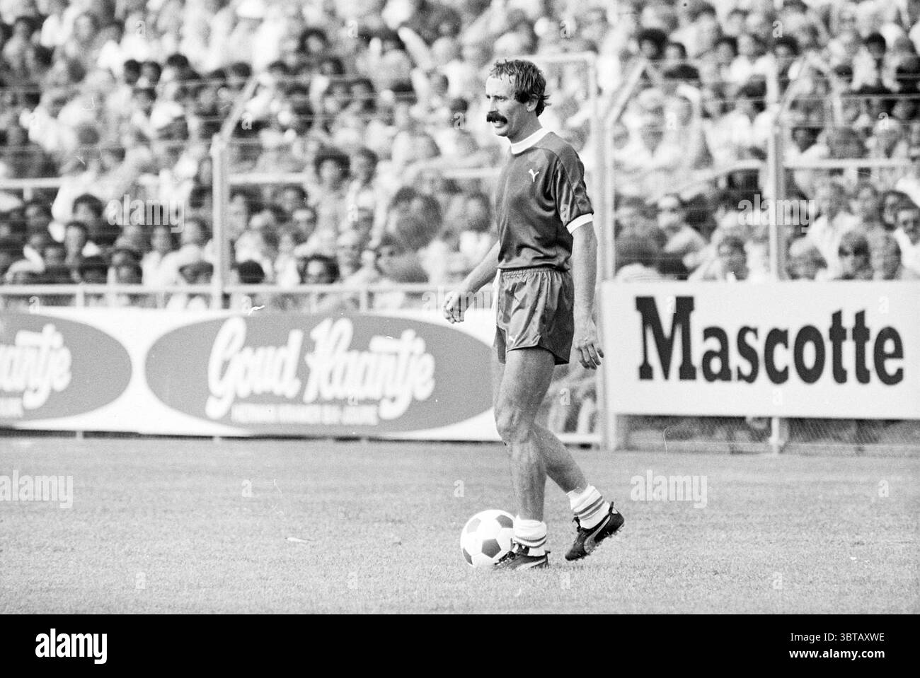 Haarlem - Robin Hood Football Haarlem, Whizgle News, Dutch Desk, Paesi Bassi, 1950 - 2000 il 15-08-1976. L'immagine include questi argomenti. La scena cattura un momento intenso su un campo da calcio, in cui un giocatore è in piedi con la palla ai suoi piedi. È vestito con una maglia scura abbinata a pantaloncini coordinati, abbinati a scarpe da calcio bianche e nere. La sua espressione facciale trasmette una concentrazione e una determinazione, amplificate da baffi distintivi che aggiungono un tocco di carattere al suo aspetto. Intorno a lui c'è un'ampia folla, raffigurata sullo sfondo, che mostra un'entusiasta spect Foto Stock