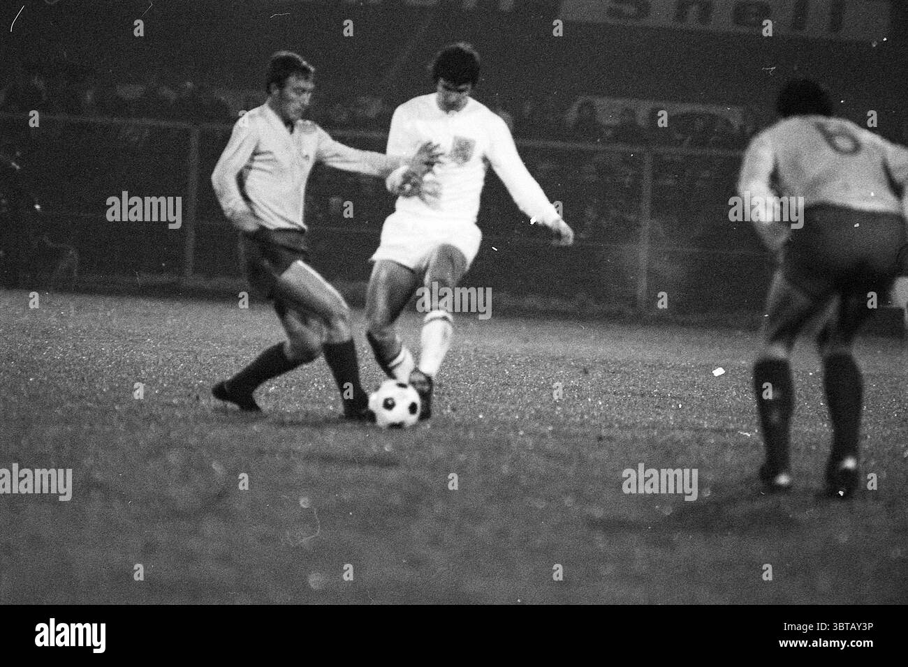 Partita di calcio Paesi Bassi., Whizgle News, Dutch Desk, Paesi Bassi, 1950 - 2000. Questi argomenti vengono visualizzati nell'immagine. La scena cattura un momento intenso su un campo di calcio durante una partita, dove l'atmosfera è carica di energia e attesa. I giocatori, vestiti con uniformi da combattimento, sono impegnati in un rapido scambio. Un atleta, indossato con una maglia bianca e pantaloncini corti, è pronto a giocare mentre manovra abilmente la palla ai suoi piedi, dimostrando concentrazione e agilità. Avversario è un altro giocatore con un'uniforme più scura e strutturata, che sta tentando di sfidare per possesso. Loro Foto Stock