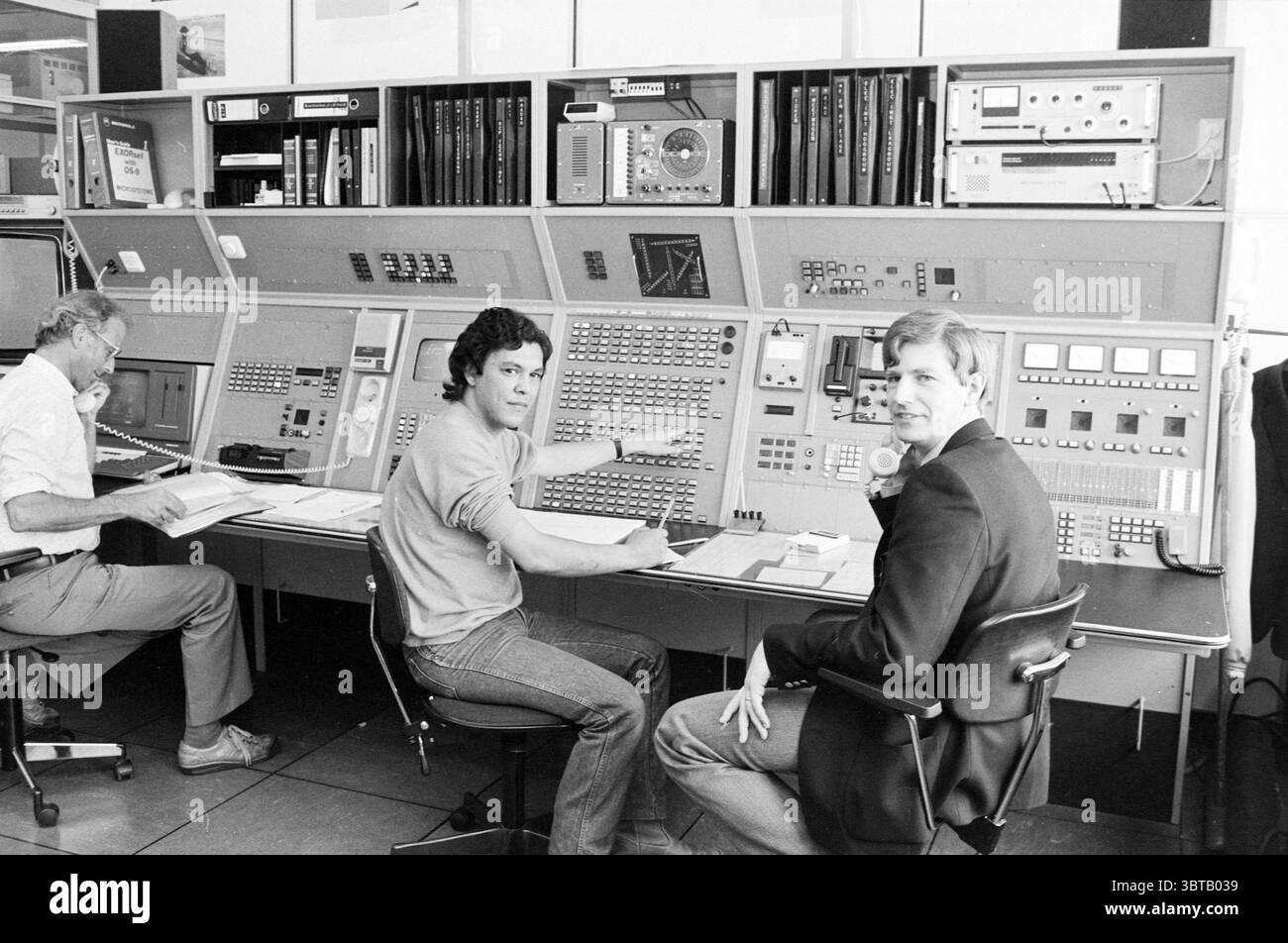 Men Lin Haring sala di controllo tecnica R.L.D. [servizio aviazione nazionale] Schiphol, Whizgle News, Dutch Desk, Paesi Bassi, 1950 - 2000 il 13-05-1985. L'immagine mostra questi argomenti. In una sala di controllo retrò-futuristica, una grande console dominava il centro, estendendosi per tutta la lunghezza della scena. La console era dotata di numerosi pulsanti, manopole e schermi, con una serie di quadranti e indicatori illuminati. La tavolozza dei colori includeva toni di grigio attenuati, accentuati da luci verdi, rosse e arancioni emesse da vari controlli, creando un'atmosfera leggermente industriale. A sinistra, Foto Stock