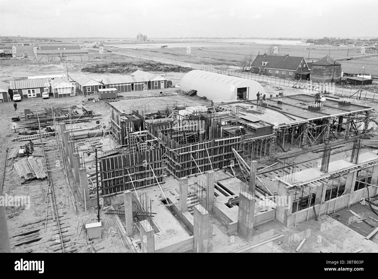 Torre d'acciaio P.T.T. PTT posta in città, Whizgle News, Dutch Desk, Paesi Bassi, 1950 - 2000 on 31-10-1967. L'immagine include questi argomenti. La scena cattura un cantiere visto da un'angolazione elevata, rivelando un layout strutturato dei materiali da costruzione e del lavoro in corso. In primo piano, numerose travi in acciaio e forme in legno sono disposte in un modello a griglia, che indica la struttura emergente di un edificio. Tavole sparse e pali di legname contribuiscono a creare un ambiente di lavoro intenso. Le persone possono essere viste in varie aree del sito, rivestite di attrezzature di sicurezza che risaltano aga Foto Stock