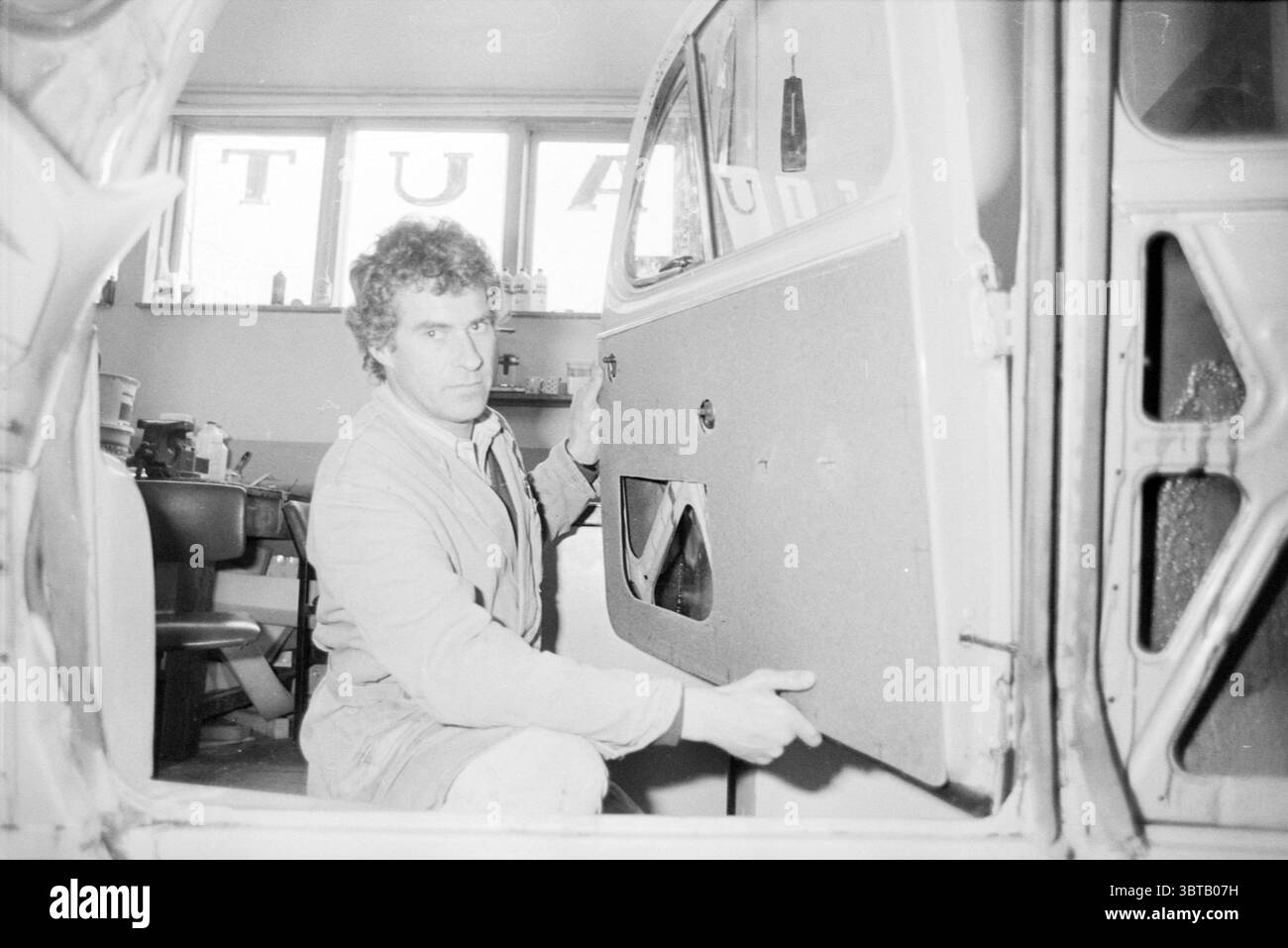 Azienda di assemblaggio porte auto garage, Whizgle News, Dutch Desk, Paesi Bassi, 1950 - 2000 il 23-04-1986. Questi argomenti vengono visualizzati nell'immagine. La scena si sviluppa in un'officina, illuminata da una luce soffusa e diffusa che crea un'atmosfera calda e invitante. Lo spazio è pieno di strumenti e attrezzature tipici di un'officina di riparazione auto, che suggeriscono attività e senso dello scopo. Un uomo è posizionato in primo piano, concentrato sul suo compito. Ha i capelli ricci e un'espressione seria, che indica la concentrazione. È vestito con una giacca da lavoro di colore chiaro, che contrasta leggermente con la Foto Stock Azienda di assemblaggio porte auto garage, Whizgle News, Dutch Desk, Paesi Bassi, 1950 - 2000 il 23-04-1986. Questi argomenti vengono visualizzati nell'immagine. La scena si sviluppa in un'officina, illuminata da una luce soffusa e diffusa che crea un'atmosfera calda e invitante. Lo spazio è pieno di strumenti e attrezzature tipici di un'officina di riparazione auto, che suggeriscono attività e senso dello scopo. Un uomo è posizionato in primo piano, concentrato sul suo compito. Ha i capelli ricci e un'espressione seria, che indica la concentrazione. È vestito con una giacca da lavoro di colore chiaro, che contrasta leggermente con la Foto Stock