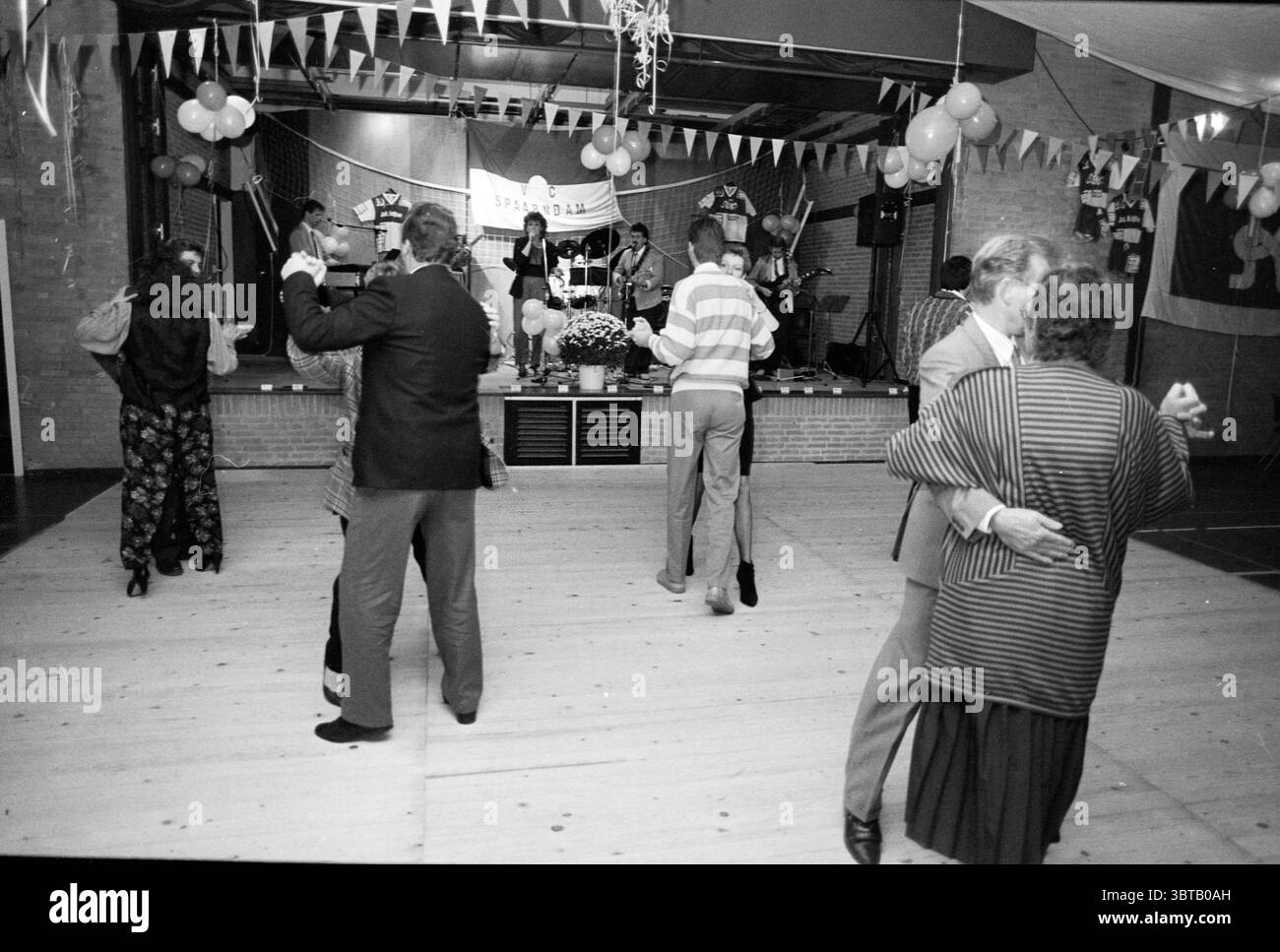 Festa del club di pallavolo nella sala del villaggio di Spaarndam Volleyball Spaarndam, Whizgle News, Dutch Desk, Paesi Bassi, 1950 - 2000 il 29-10-1988. Questi sono gli argomenti nell'immagine. La scena cattura un vivace raduno che si svolge in una sala adornata con decorazioni colorate. L'atmosfera è festosa, caratterizzata da un senso di gioia e movimento. In primo piano, diverse coppie sono impegnate nella danza, aggiungendo un elemento dinamico alla scena. Il loro abbigliamento varia nello stile, con alcuni individui vestiti in abbigliamento formale, mentre altri optano per abiti più casual. Un uomo con un vestito oscuro si vede Twirlin Foto Stock