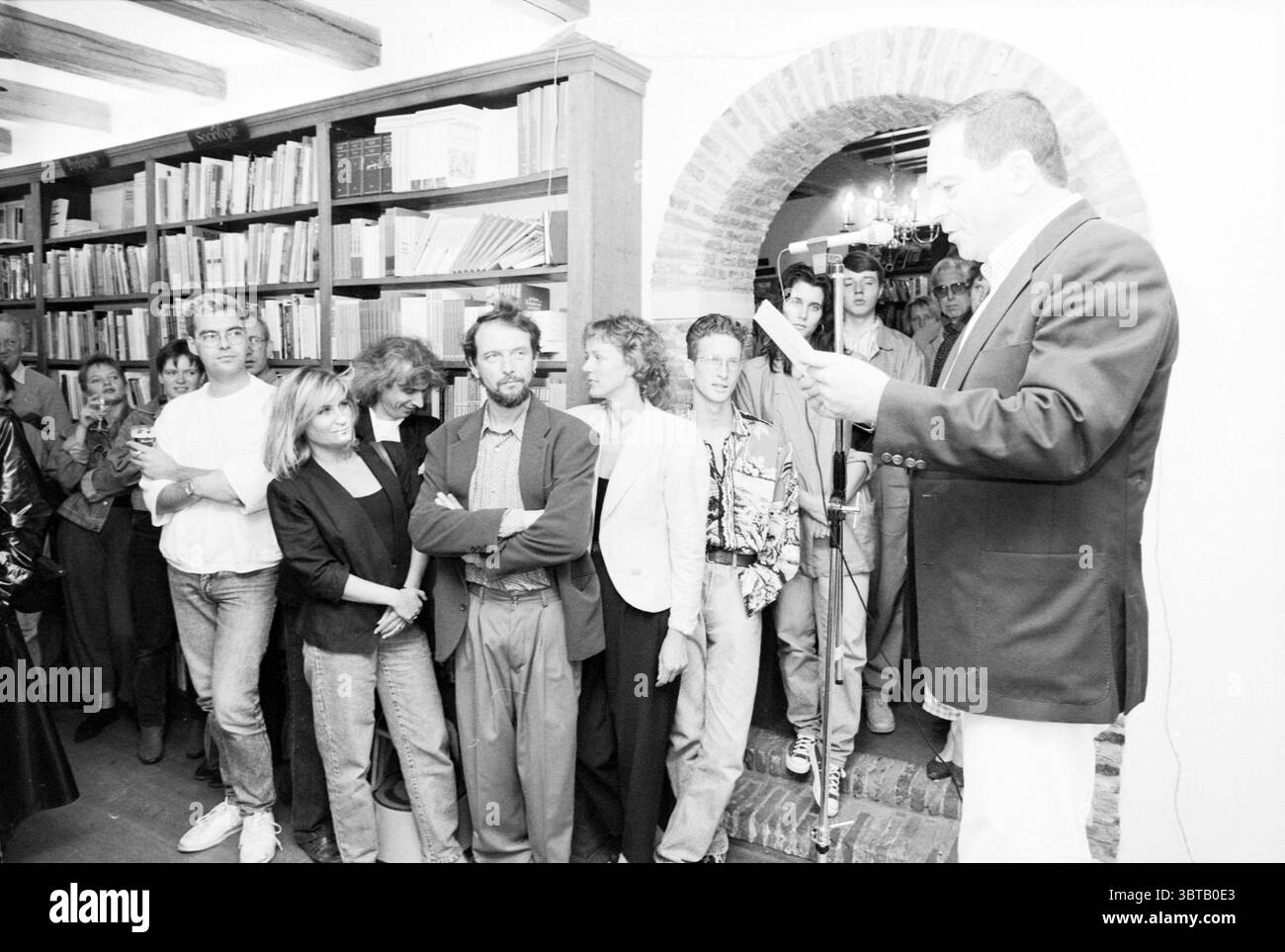 Presentazione del libro di Lennaert Nijgh libri e librai presentazione, Whizgle News, Dutch Desk, Paesi Bassi, 1950 - 2000 il 23-09-1989. Questi argomenti vengono visualizzati nell'immagine. La scena cattura un vivace raduno in un ambiente intimo e pieno di libri. A sinistra, un uomo si trova davanti a un microfono sullo sfondo di librerie rivestite di vari volumi, creando un'atmosfera intellettuale. È vestito con un blazer scuro e sembra leggere con un focus che suggerisce di essere impegnato con il suo pubblico. Di fronte a lui, un gruppo eterogeneo di individui, sia uomini che donne, ascoltano attentamente. Foto Stock