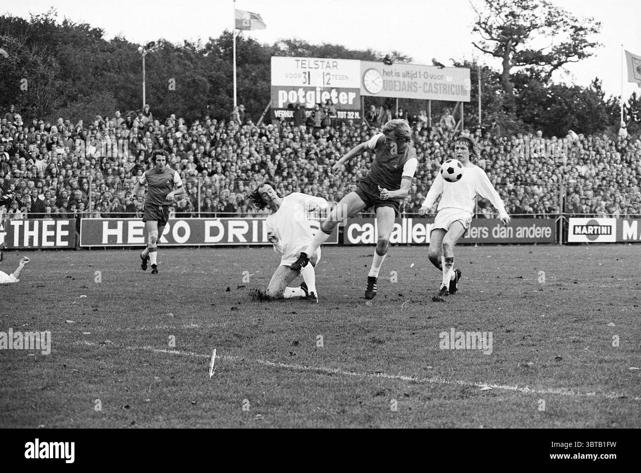 Football Telstar-Feijenoord Haarlem Jan Gijzenkade Paesi Bassi, Whizgle News, Dutch Desk, Paesi Bassi, 1950 - 2000 il 22-10-1973. Questi argomenti vengono visualizzati nell'immagine. La scena cattura un momento dinamico su un campo erboso durante una partita di calcio, incapsulando movimento e intensità. In primo piano, due giocatori sono impegnati in un'interazione critica: Uno, in una maglia rossa, salta sopra un avversario vestito di bianco che si trova a terra, tentando di riprendere possesso della palla. Il giocatore in rosso mostra atleticità, il suo corpo è posizionato per colpire o controllare la palla, mostrando un determinato Foto Stock