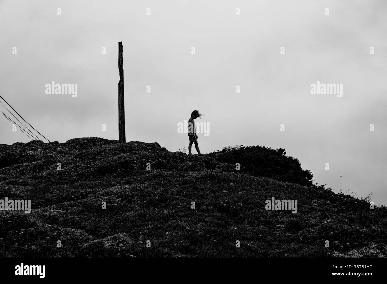 Figura solitaria che cammina lungo le colline spazzate dal vento di Nazaré in bianco e nero Foto Stock