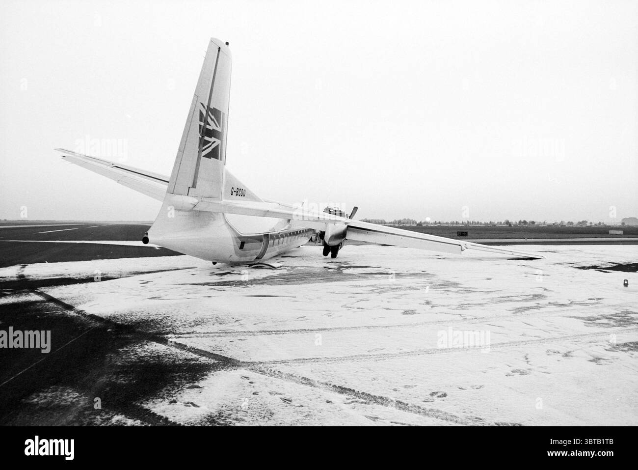 Atterraggio di emergenza di un Air UK Fokker27 a Schiphol alla stampa Schiphol, Whizgle News, Dutch Desk, Paesi Bassi, 1950 - 2000 il 19-07-1990. Questi sono gli elementi dell'immagine. La scena presenta un aereo ad elica posizionato su una pista innevata, che crea un contrasto sorprendente con l'ambiente silenzioso. L'aereo, prevalentemente bianco con sfumature di blu e un motivo con bandiera Union Jack sulla coda, appare un po' intemprato, evidenziando la sua presenza sullo sfondo squallido. Intorno all'aereo, un sottile strato di neve ricopre il terreno, suggerendo un'atmosfera fredda e ventosa. TH Foto Stock