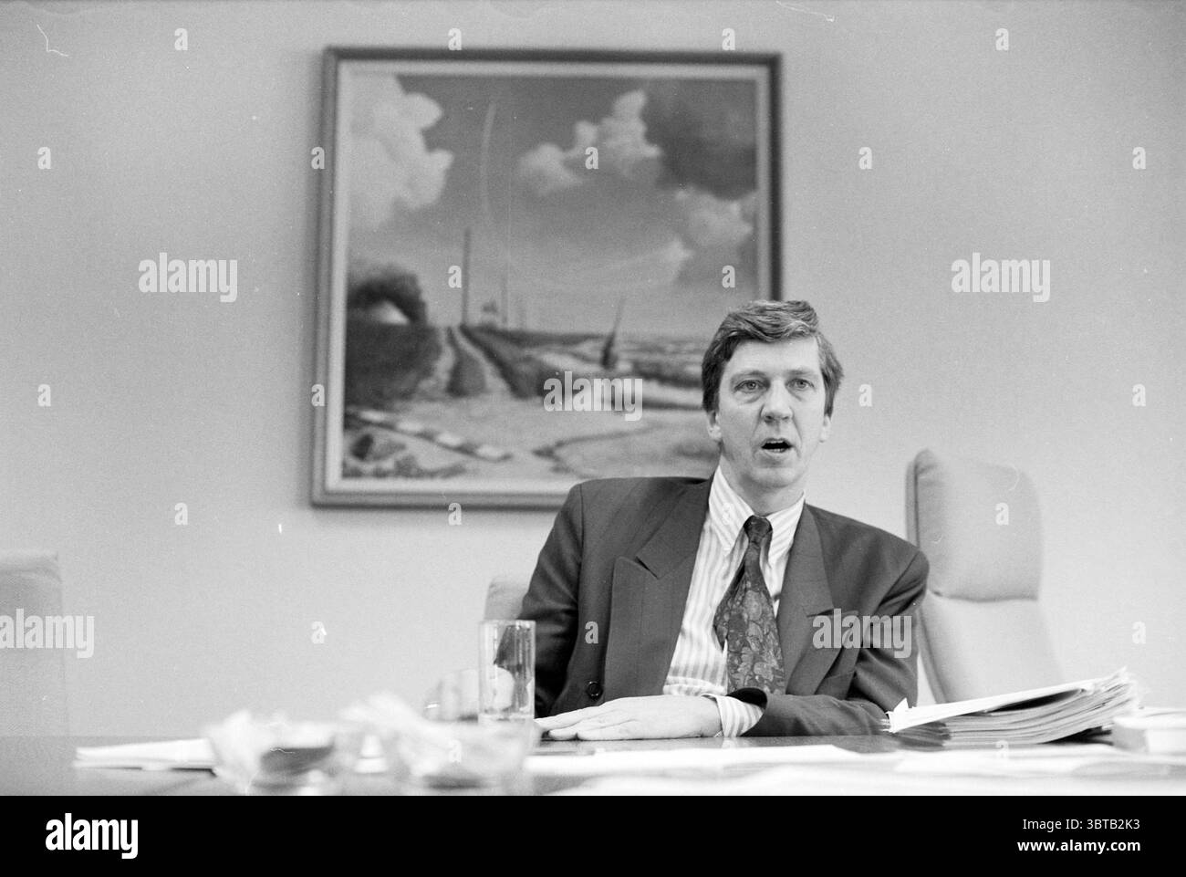 Consigliere Jaap Kroon comune di Haarlemmermeer in relazione al piano di politica ambientale municipale 1991 Hoofddorp Raadhuisplein Paesi Bassi, Whizgle News, Dutch Desk, Paesi Bassi, 1950 - 2000 il 05-11-1991. L'immagine include questi argomenti. La scena vede un uomo seduto a una scrivania, che sembra impegnato in una conversazione o in una discussione. È vestito con una tuta scura formale completata da una camicia bianca e blu a righe e da una cravatta a motivi, suggerendo un ambiente professionale. La sua espressione trasmette la concentrazione, forse indicando un tono serio o ponderato. Sulla scrivania prima di lui Foto Stock