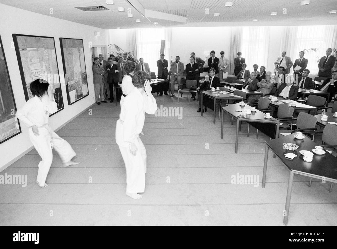 Riunione del Dutch Korean Trade Club con dimostrazione di taekwondo, Whizgle News, Dutch Desk, Paesi Bassi, 1950 - 2000 il 14-09-1989. Questi argomenti vengono visualizzati nell'immagine. La scena cattura un ambiente interno formale, probabilmente una sala conferenze o un ambiente simile. Le pareti sono adornate da grandi opere d'arte astratte che introducono colori audaci come rossi, blu e gialli, fornendo un contrasto sorprendente con la stanza altrimenti dai toni neutrali. In primo piano, due individui sono impegnati in una dimostrazione di arti marziali, vestiti con i tradizionali gi bianchi. I loro movimenti sono dinamici e precisi, Foto Stock