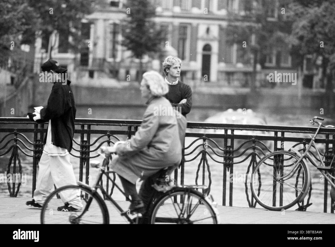 Giocatore di baseball E. Fokke, Whizgle News, Dutch Desk, Paesi Bassi, 1950 - 2000 on 26-09-1994. L'immagine mostra questi argomenti. La scena presenta un vivace ambiente urbano lungo un canale, caratterizzato da un mix di movimento e quiete. A sinistra, una persona con abiti scuri cammina a tutta velocità, tenendo una bevanda calda, magari un caffè, mentre la brezza si arriccia il berretto. Hanno un'espressione concentrata, che suggerisce di essere in viaggio verso una destinazione. Al centro, un altro individuo si erge con una postura premurosa, braccia incrociate, guardando l'acqua. I loro capelli dai colori più chiari contrastano con Foto Stock