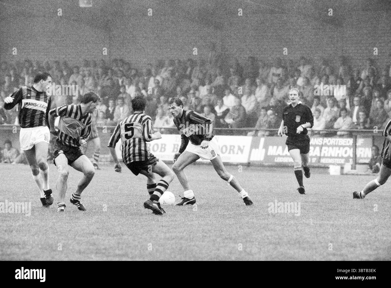 RCH - Wilhelmus Football R.C.H., Whizgle News, Dutch Desk, Paesi Bassi, 1950 - 2000 il 11-09-1988. Questi argomenti sono mostrati nell'immagine. La scena cattura un momento dinamico su un campo da calcio, pieno di azione e intensità. In primo piano, diversi giocatori sono impegnati in un gioco competitivo. Sono presenti due atleti, uno che dribbling abilmente la palla mentre l'altro, contrassegnato da una maglia a strisce, tenta di intercettarla. I giocatori mostrano una gamma di atletismo e concentrazione, le loro espressioni rivelano determinazione e concentrazione. Gli atleti sono vestiti in unifo a contrasto Foto Stock