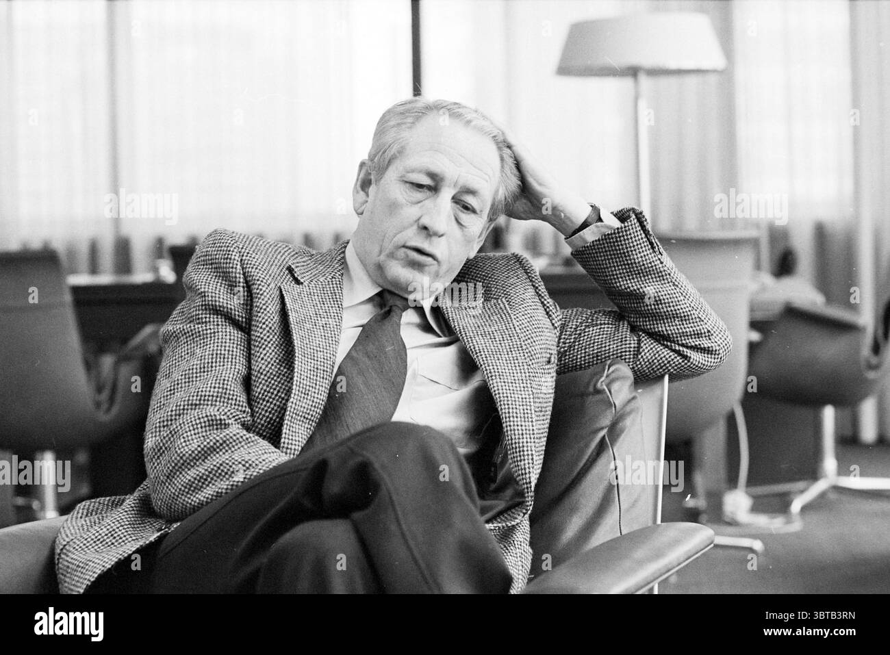 Direttore Estel HR. Highland BLAST Fornaces Portraits, Whizgle News, Dutch Desk, Paesi Bassi, 1950 - 2000 il 23-02-1981. L'immagine mostra questi argomenti. La scena raffigura un uomo seduto su una sedia moderna ed elegante. Sembra essere profondo nel pensiero, con un'espressione contemplativa sul suo volto. I suoi capelli sono grigi, e ha un comportamento un po' stanco, suggerendo che potrebbe riflettere su un argomento o momento significativo. È vestito con un classico blazer in tweed grigio abbinato a una camicia con colletto e una cravatta, che aggiunge un tocco di raffinatezza al suo aspetto. Il contrasto tra la texture o Foto Stock