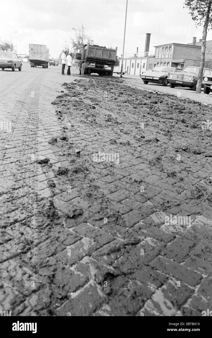Ingoiare sulle strade Oudeweg costruzione di strade piantando Haarlem Oudeweg Paesi Bassi, Whizgle News, Dutch Desk, Paesi Bassi, 1950 - 2000 il 16-10-1978. L'immagine contiene questi argomenti. La scena presenta una strada che sembra fortemente influenzata da fango o sporco, creando una superficie ruvida e irregolare sui ciottoli. Il ricco colore marrone scuro del terreno contrasta con i toni più chiari delle pietre, sottolineando la rottura causata dal muck. Sullo sfondo, diversi veicoli sono parcheggiati lungo il lato della strada, aggiungendo un senso di vita quotidiana all'ambientazione. Due individui ar Foto Stock