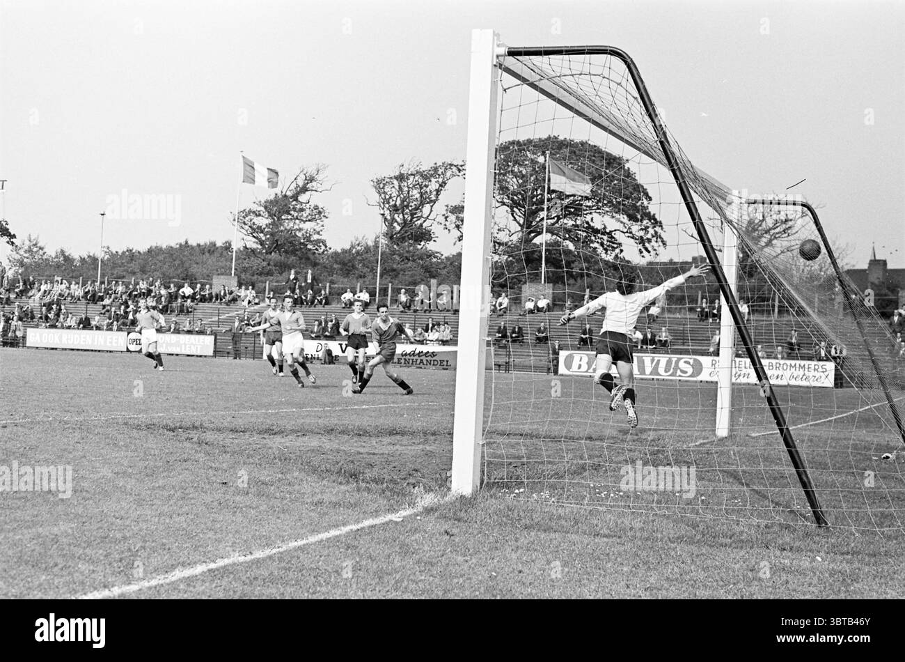 Telstar partita di calcio Velsen., Whizgle News, Dutch Desk, Paesi Bassi, 1950 - 2000. Questi sono gli argomenti nell'immagine. La scena cattura un momento dinamico su un campo sportivo, dove l'energia di una partita di calcio è palpabile. Due squadre sono impegnate in gioco, con giocatori in divise distinte che spingono verso l'obiettivo. Un giocatore, posizionato a destra, è a metà corsa, le gambe sono in movimento mentre guarda la palla, che si trova proprio di fronte a lui. La cornice della porta si trova in primo piano, i suoi pali bianchi contrastano nettamente con l'erba verde, mentre la rete si estende saldamente, catturando Foto Stock